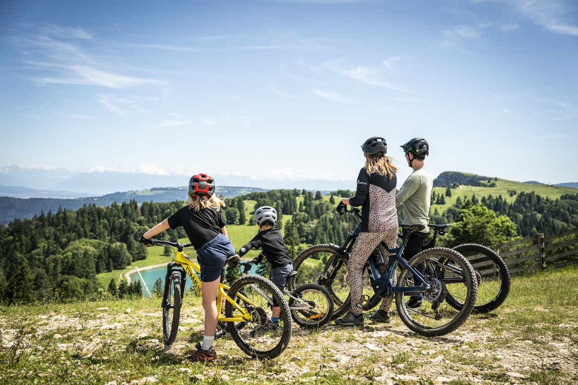 Famille en vtt regarde l'horizon et la chaîne des alpes depuis le sommet du morond