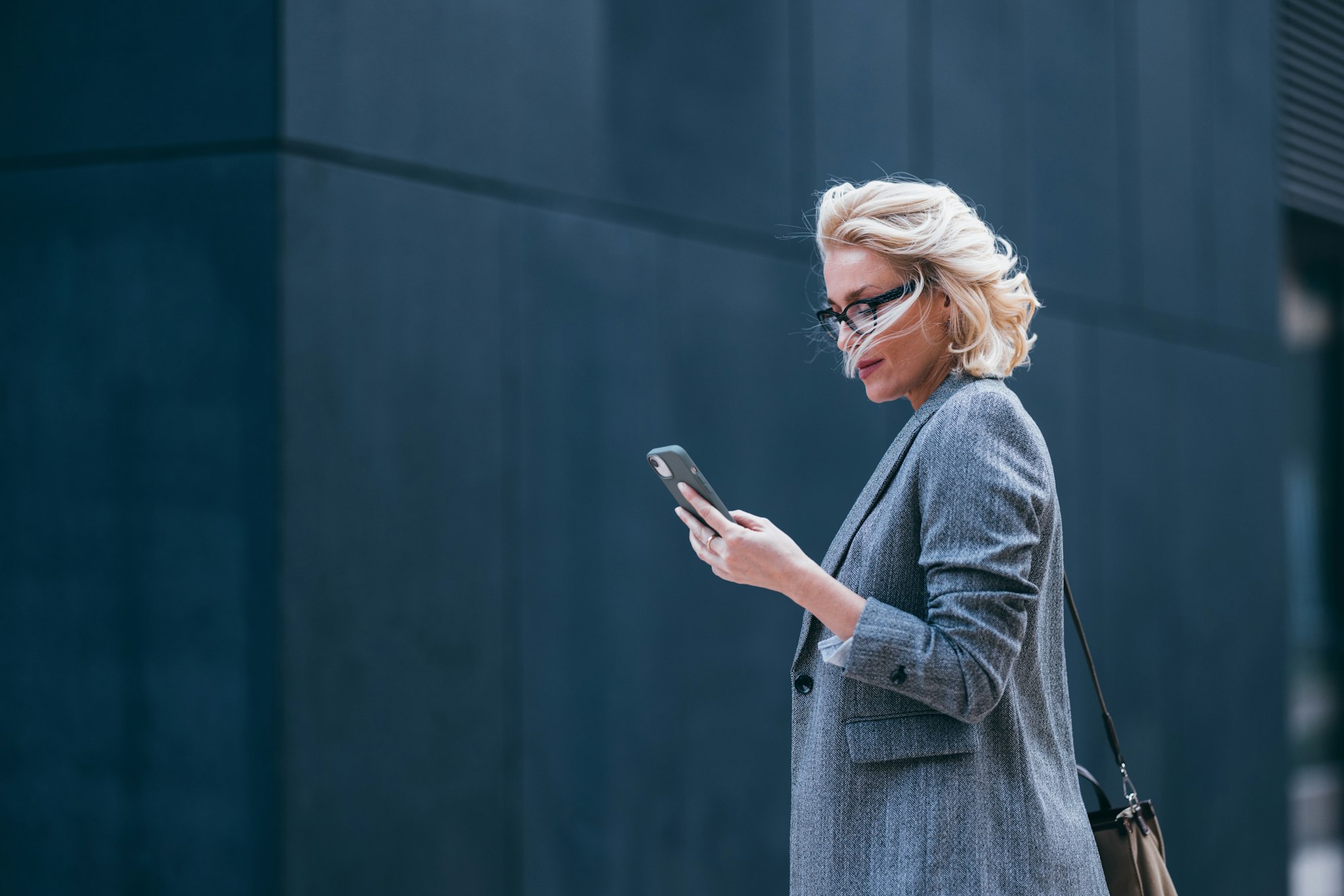 Blonde Frau läuft mit Smartphone durch die Stadt.