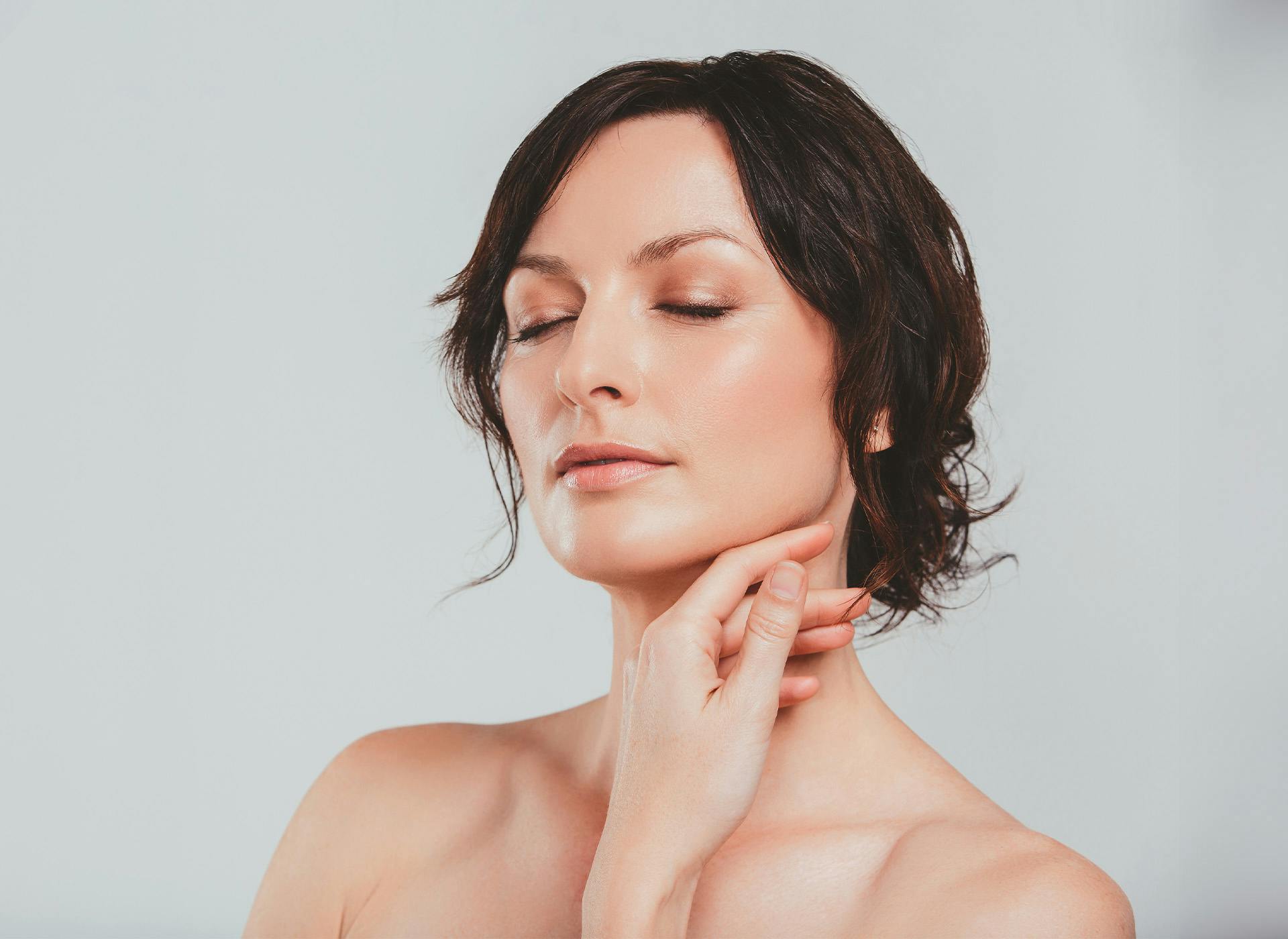 woman with eyes closed touching chin