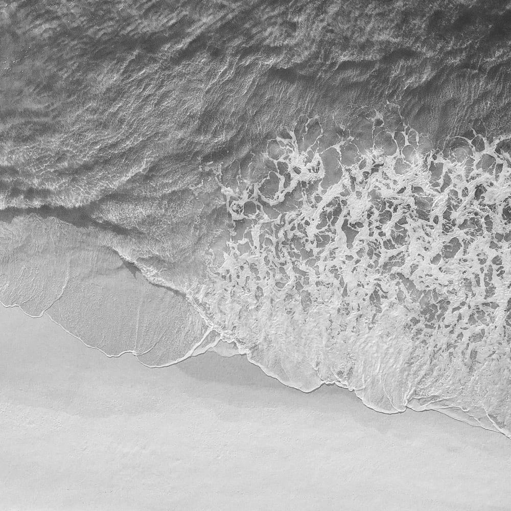 greyscale of the ocean and the sand meeting