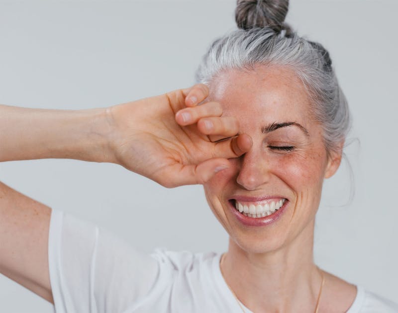 woman smiling and putting her hand over her eye