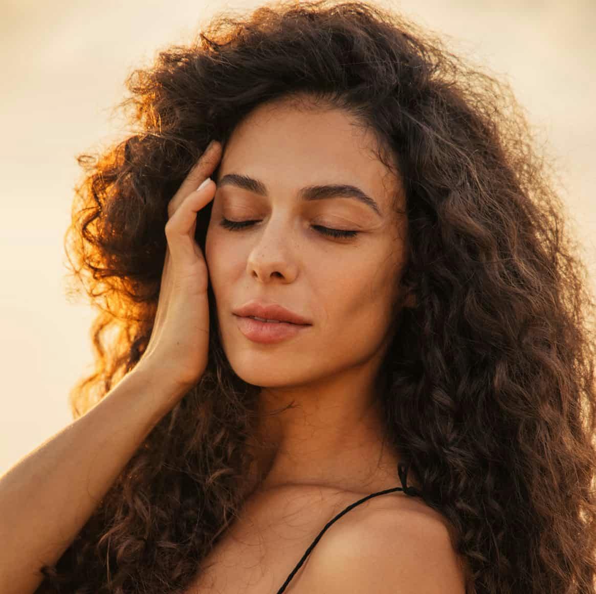 woman with very curly dark hair closing her eyes