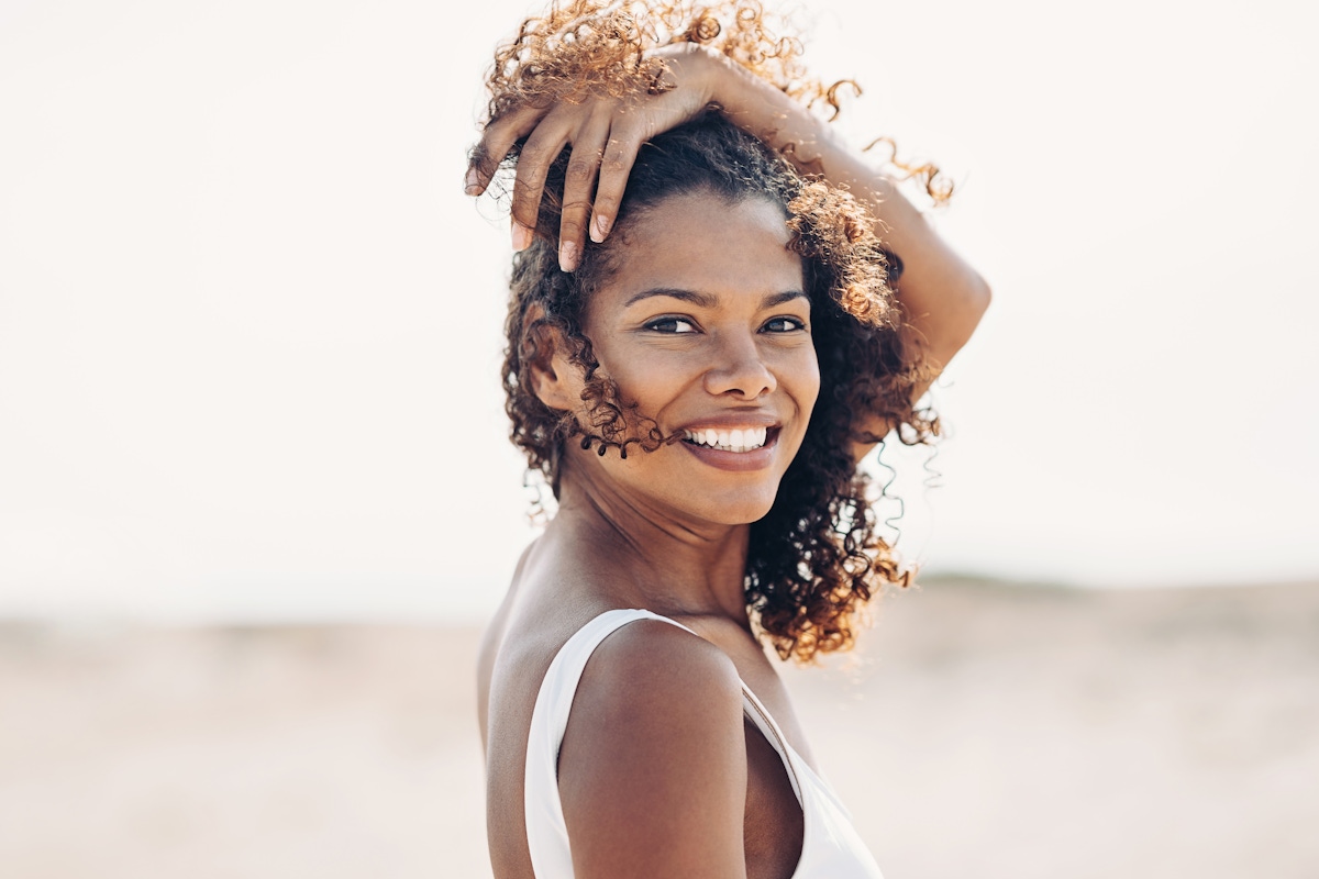 Woman at beach with hand in hair.