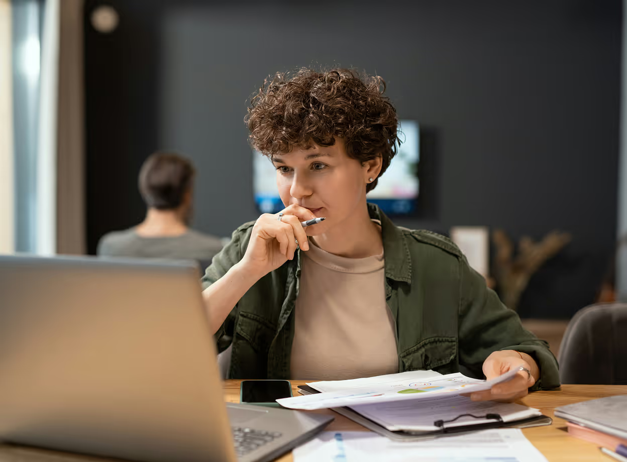 Mitarbeiterin prüft konzentriert Unterlagen am Laptop im Büro – mögliche Ursachen für einen Verstoß gegen das Arbeitszeitgesetz im Arbeitsalltag.