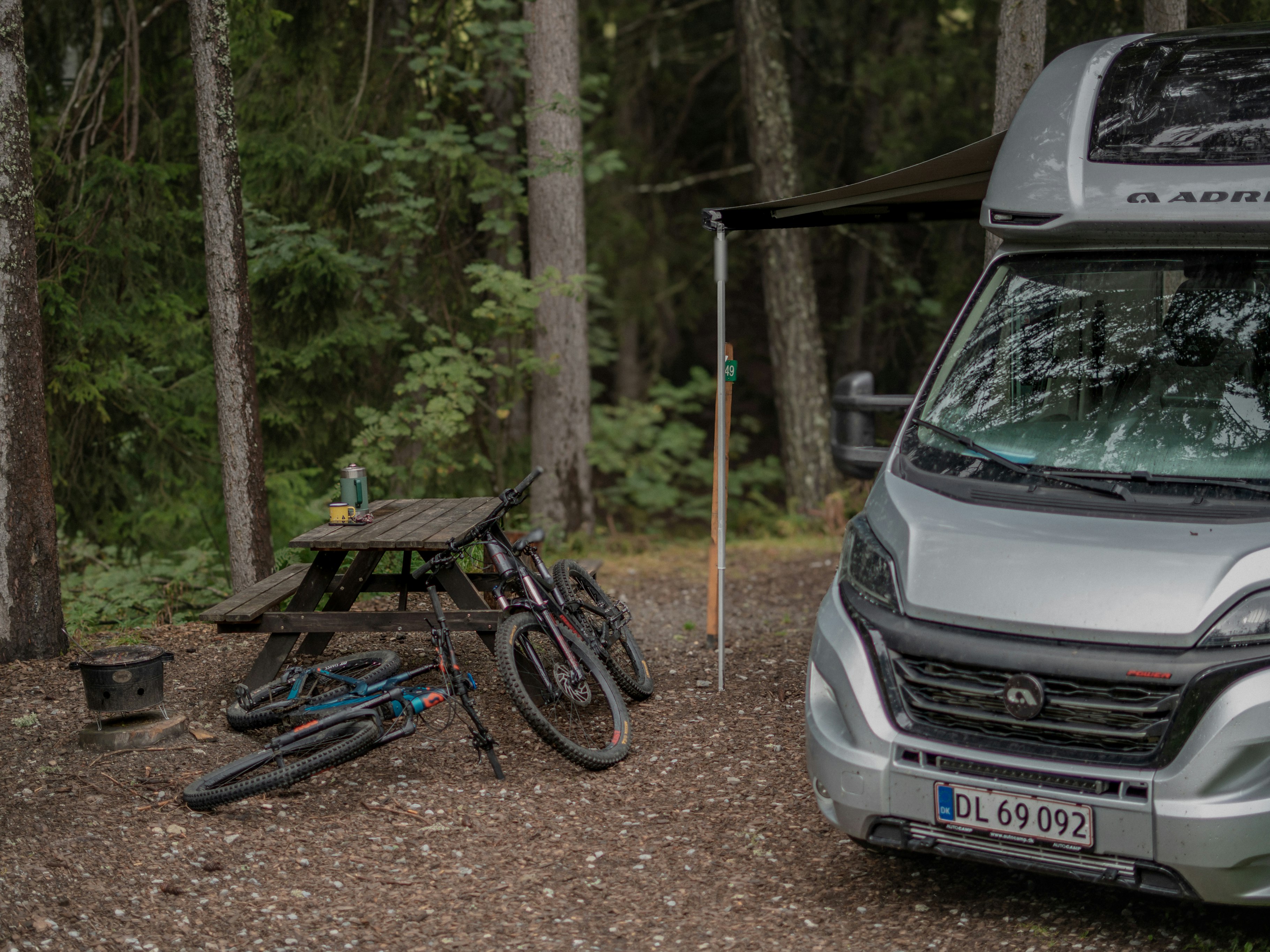 Campervan mit Bikes im Wald Grauer Campervan mit Vordach und zwei Bikes im Tannenwald auf dem Campingplatz.