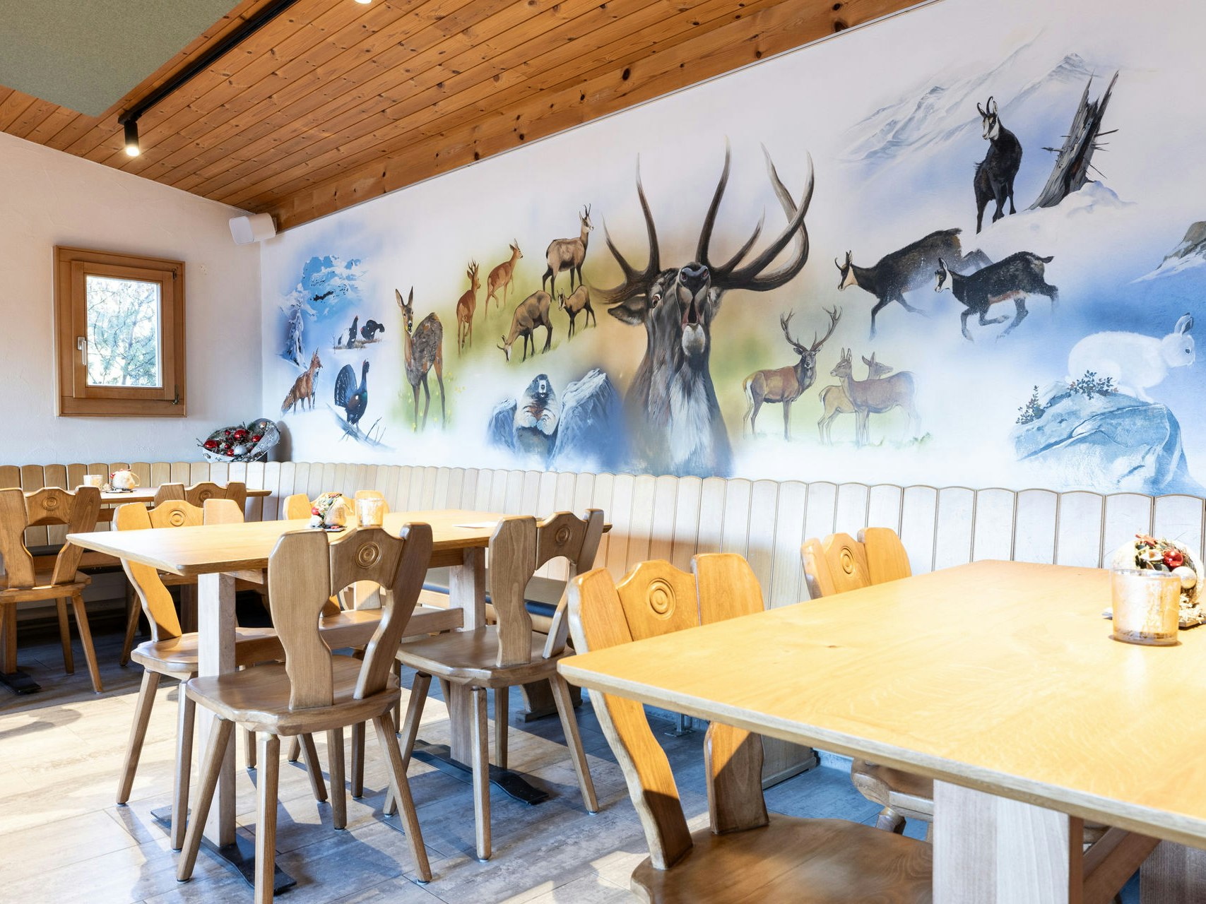 Restaurant St. Cassian Tische unter Wandbild mit Wildtieren im Restaurant