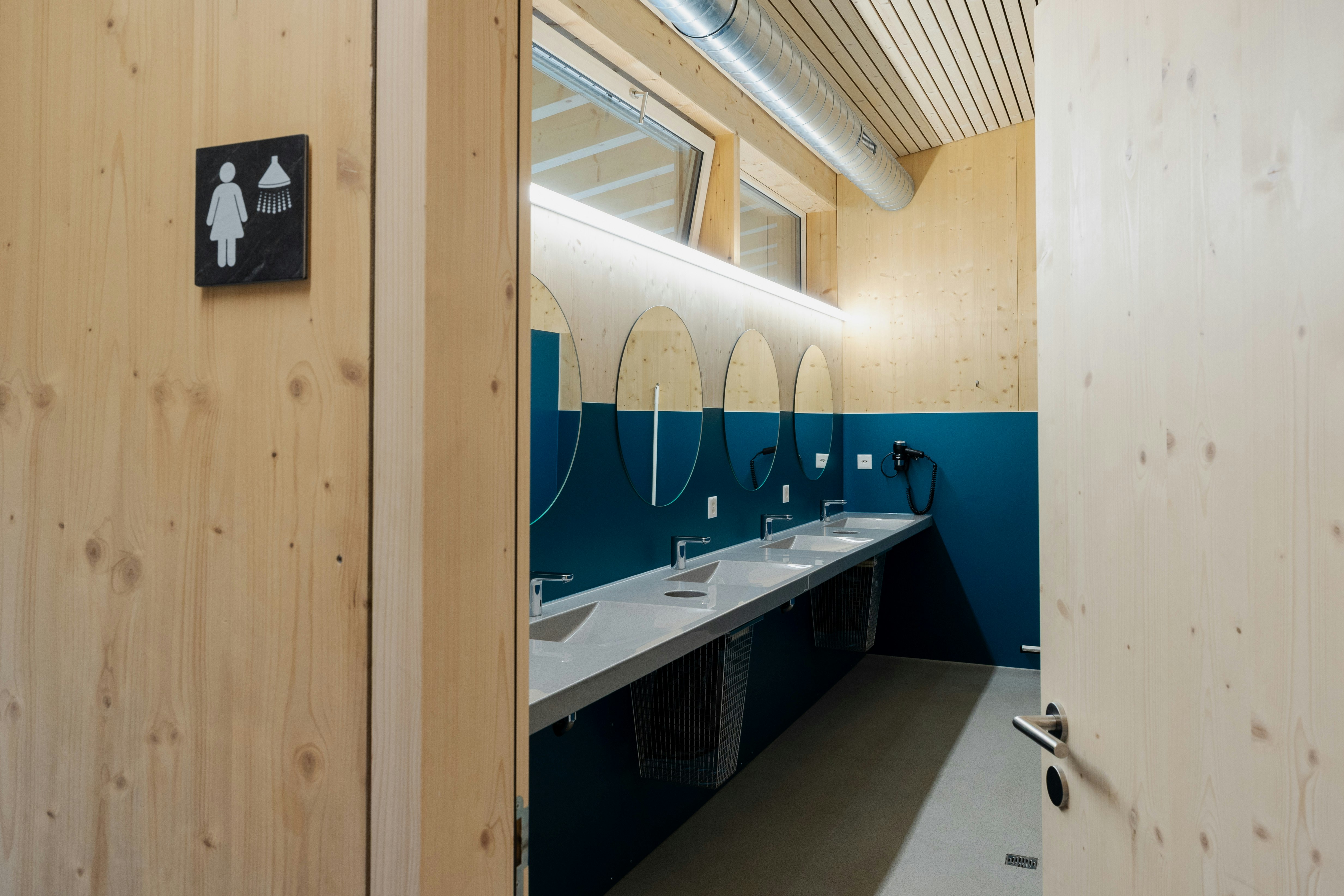Waschraum mit Holz und blauen Fliesen, Rollstuhlsymbol an der Wand, Camping Gravas