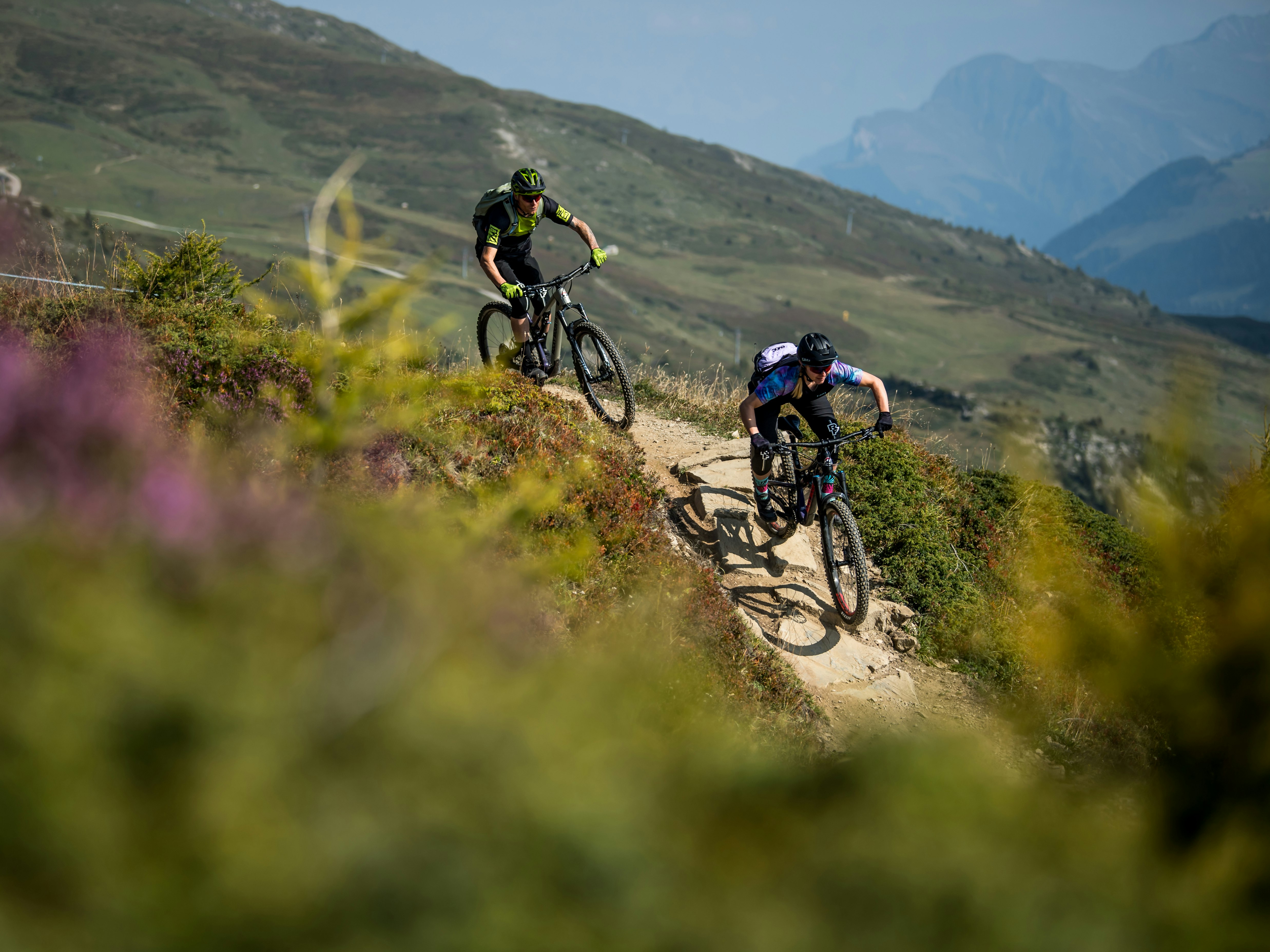 Biketour Lenzerheide Zwei Mountainbiker fahren durch eine blühende Bergwiese