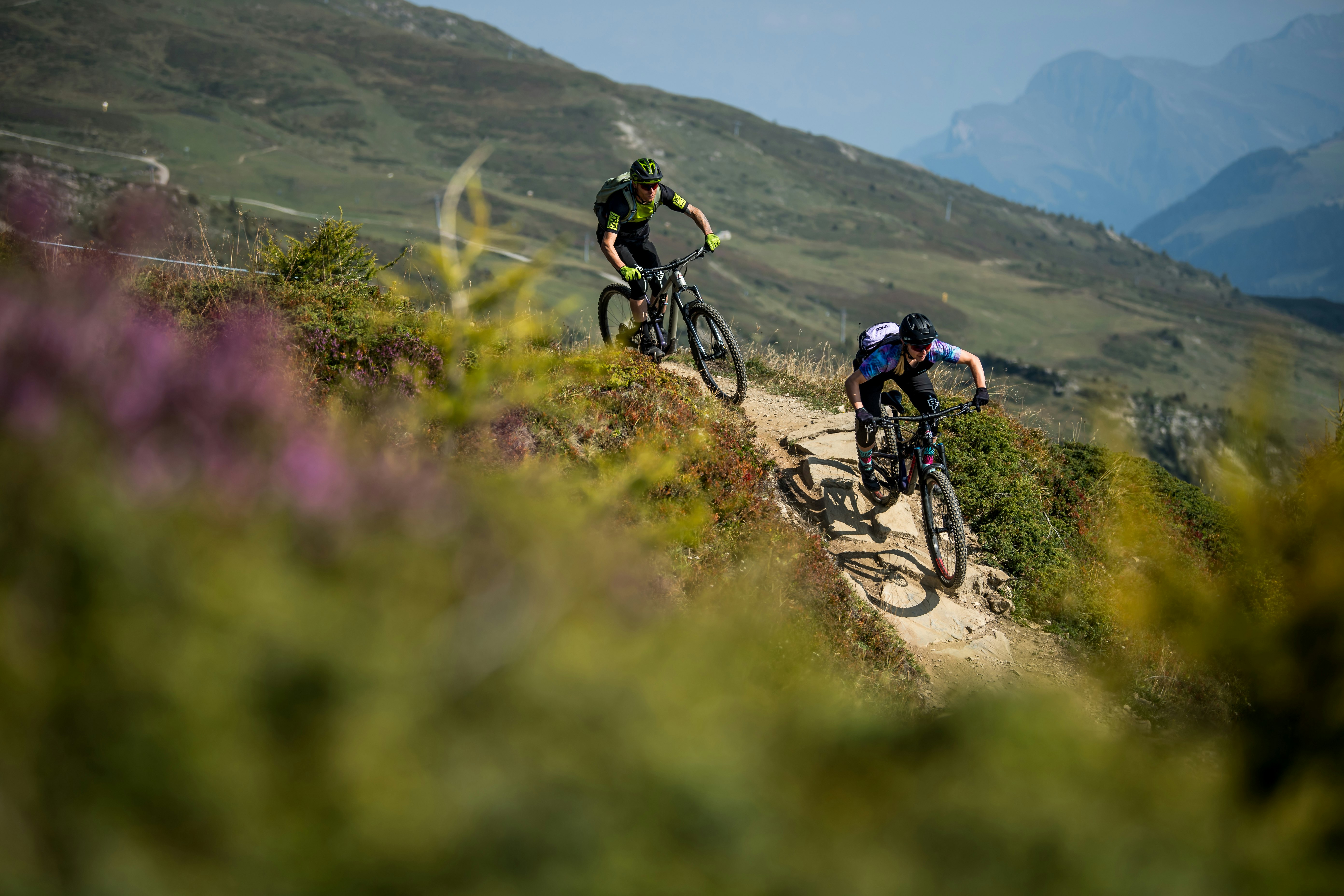Biketour Lenzerheide Zwei Mountainbiker fahren durch eine blühende Bergwiese