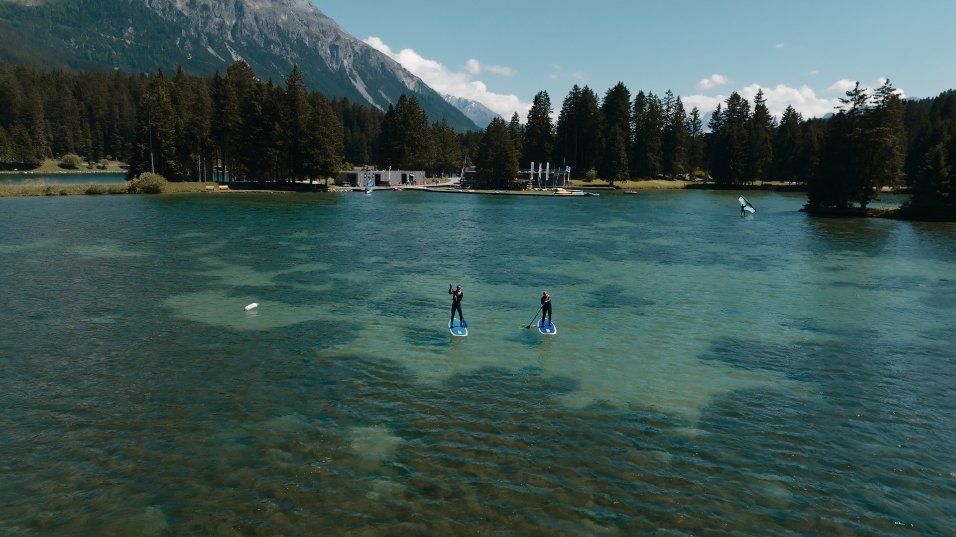 Klarer Bergsee umgeben von dichtem Nadelwald und SUPs