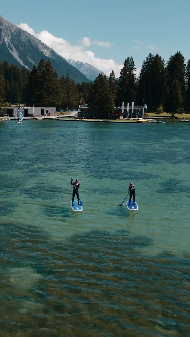Heidsee Lenzerheide Klarer Bergsee umgeben von dichtem Nadelwald und SUPs