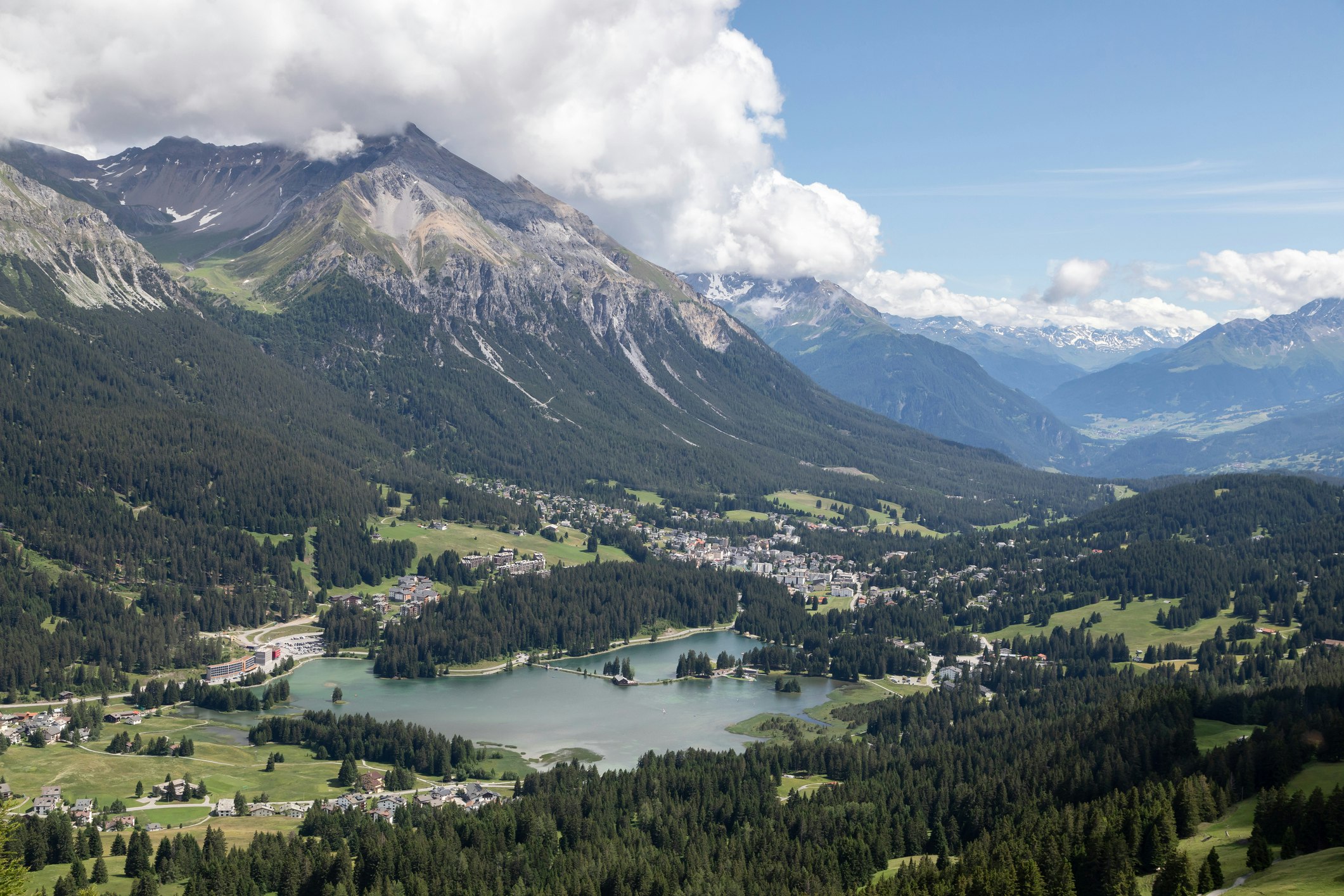 Türkisfarbener Bergsee umgeben von grünen Wäldern und Gipfeln