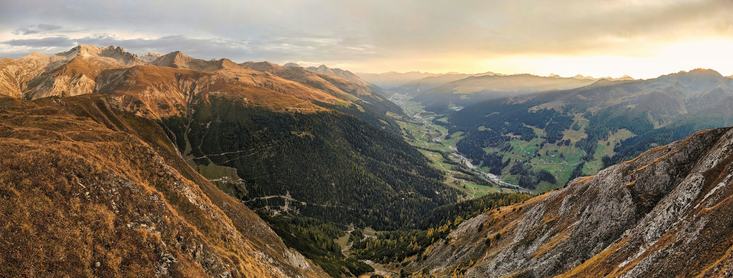Bergtal in warmem Abendlicht mit Nebelschwaden über den Gipfeln