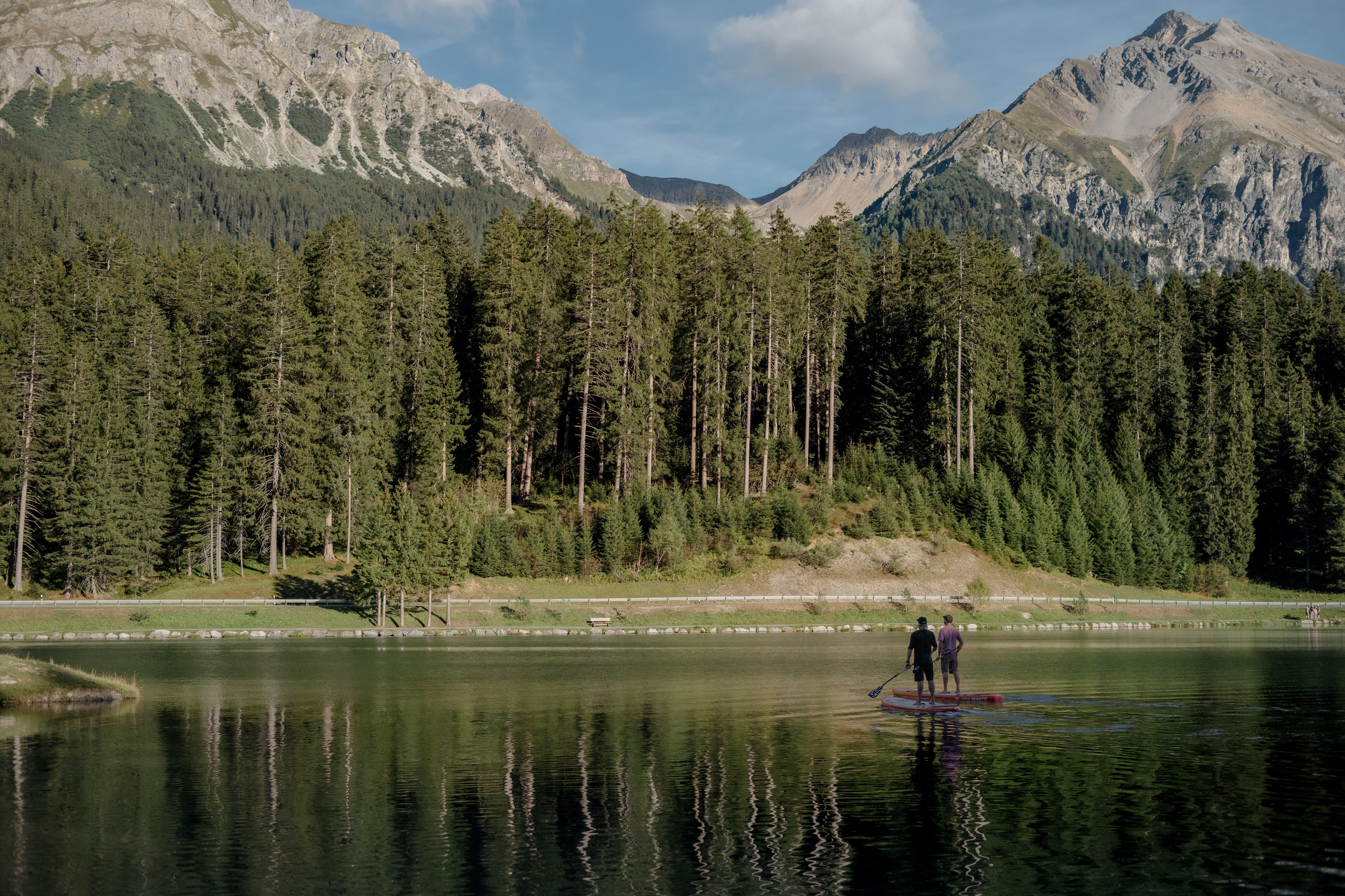 Bergsee mit Bergpanorama im Hintergrund und zwei Leute auf dem SUP