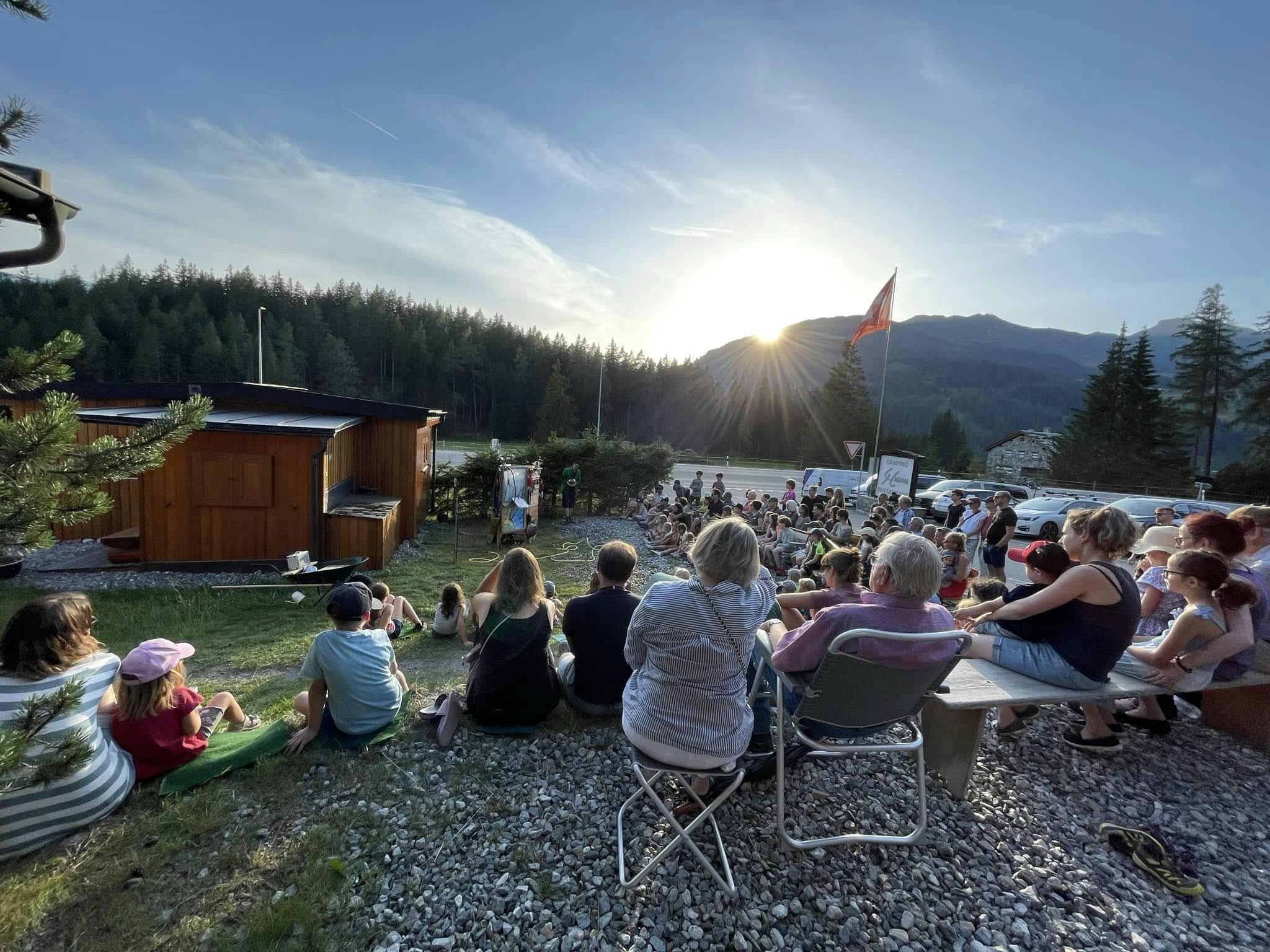 Gäste geniessen eine Veranstaltung auf dem Campingplatz bei Sonnenuntergang