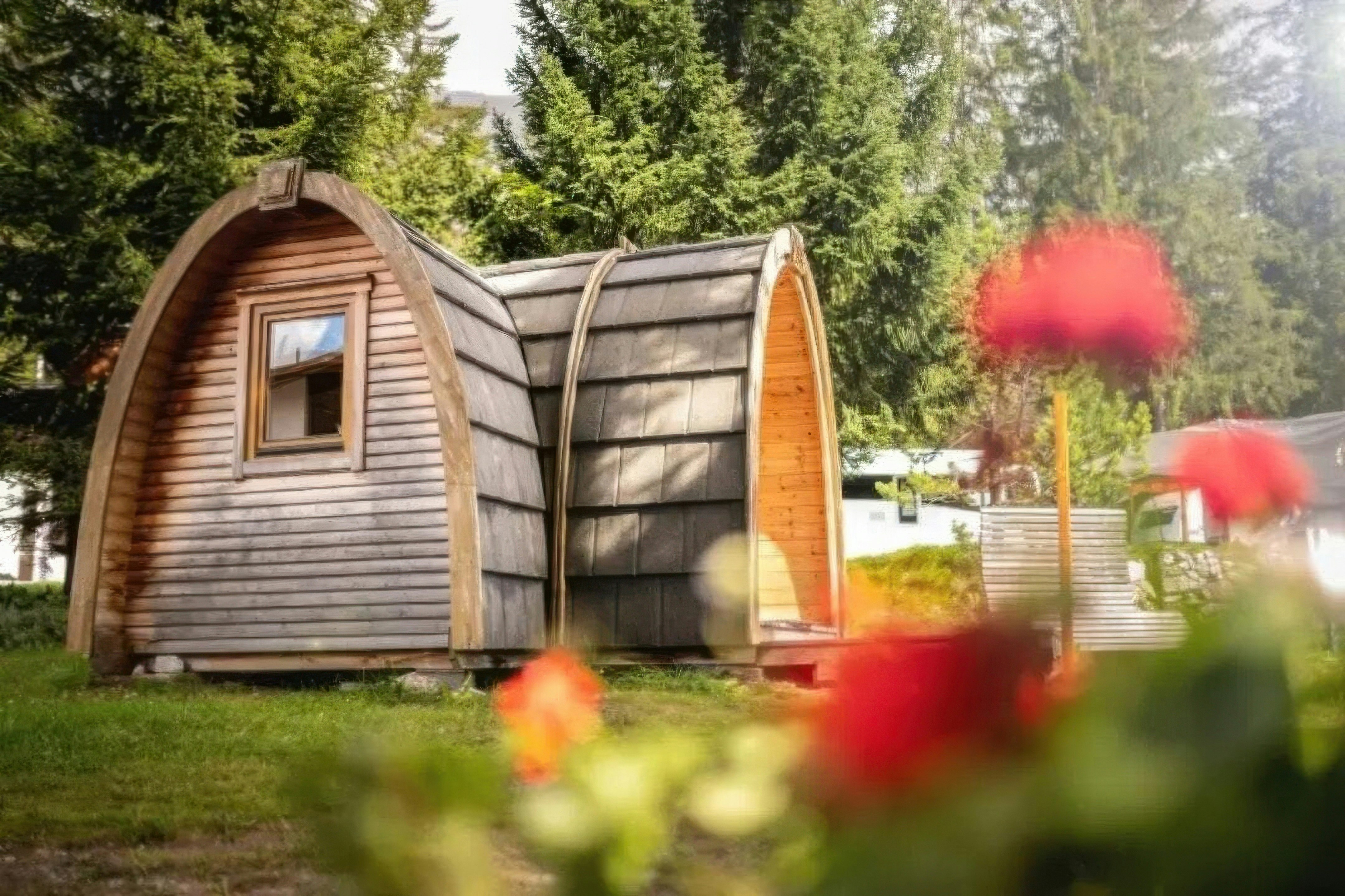 Rustikale Camping-Pod-Hütte umgeben von blühenden Blumen im Sommer