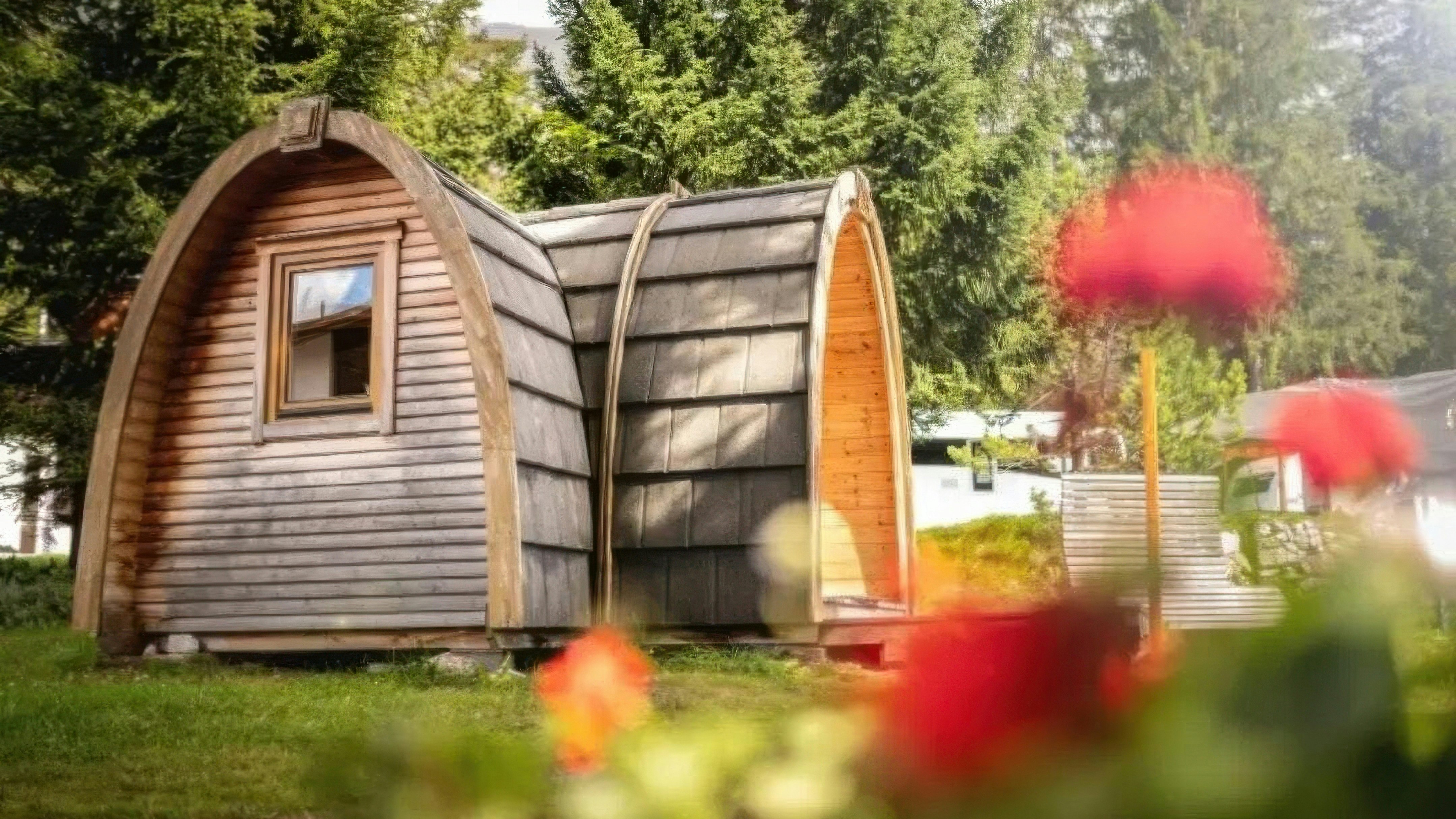 Camping St. Cassian Holziglu Rustikale Camping-Pod-Hütte umgeben von blühenden Blumen im Sommer