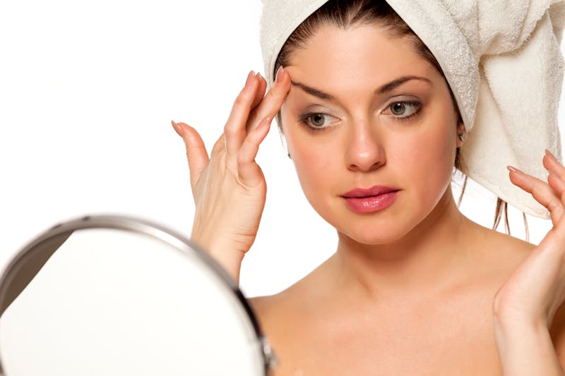 woman looking in the mirror touching her eyebrow