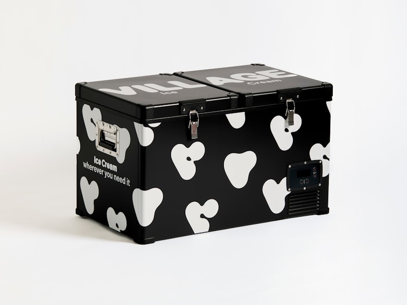 A black portable freezer with white cow-like spots and the text ice cream wherever you need it printed on the side, placed against a plain white background.