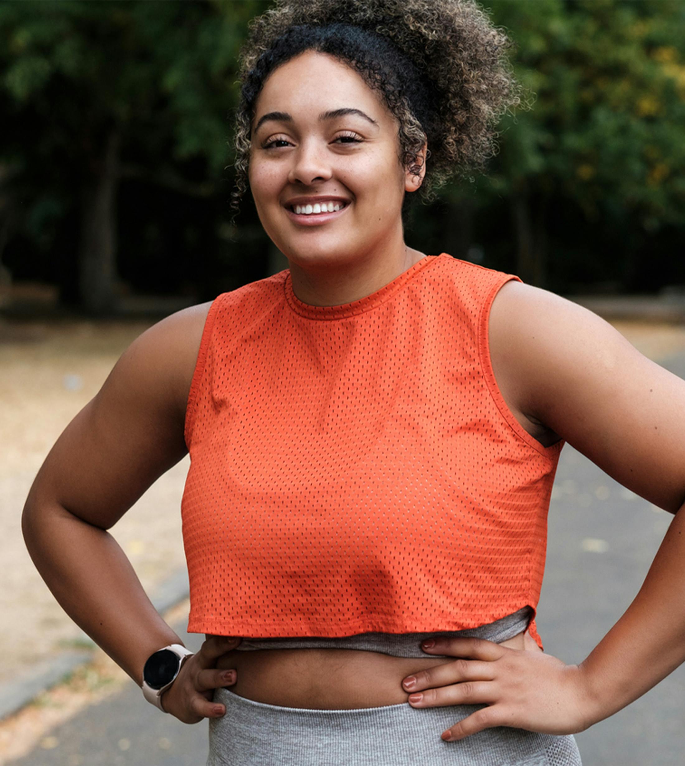 woman in orange shirt smiling with hands on hips outside
