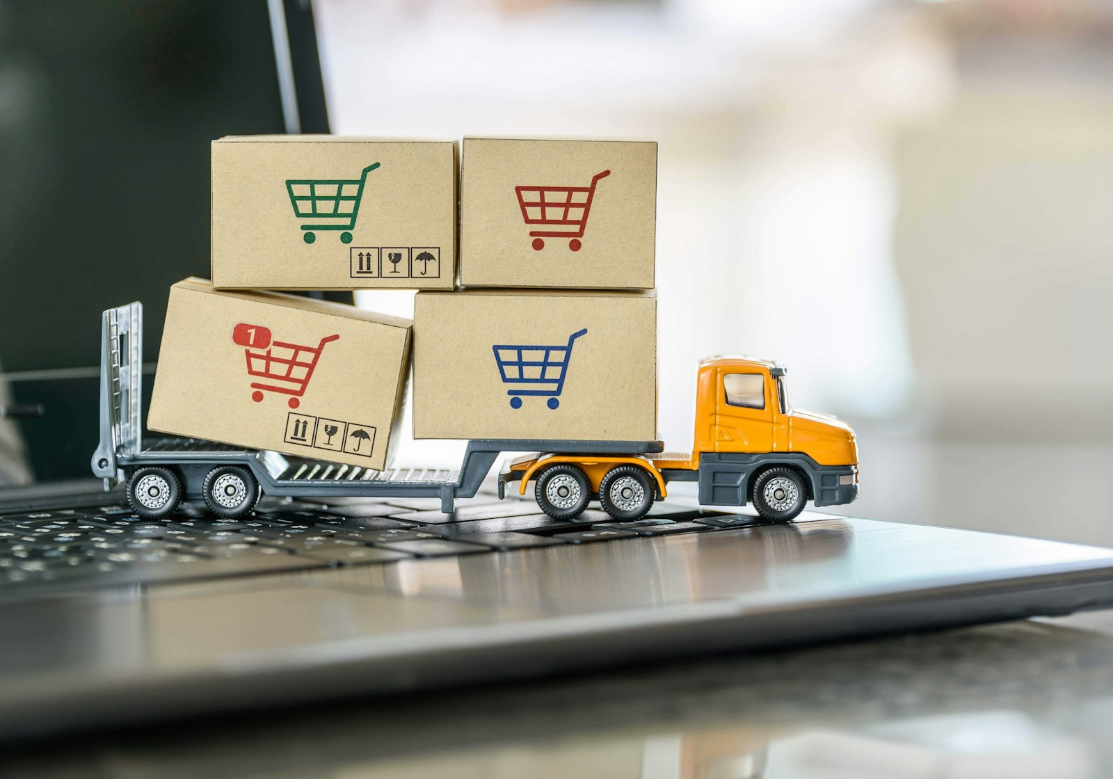 Illustration of a small delivery truck carrying boxes with shopping cart icons driving across a laptop keyboard, representing ShipHawk integrations with WooCommerce and Microsoft Dynamics 365.