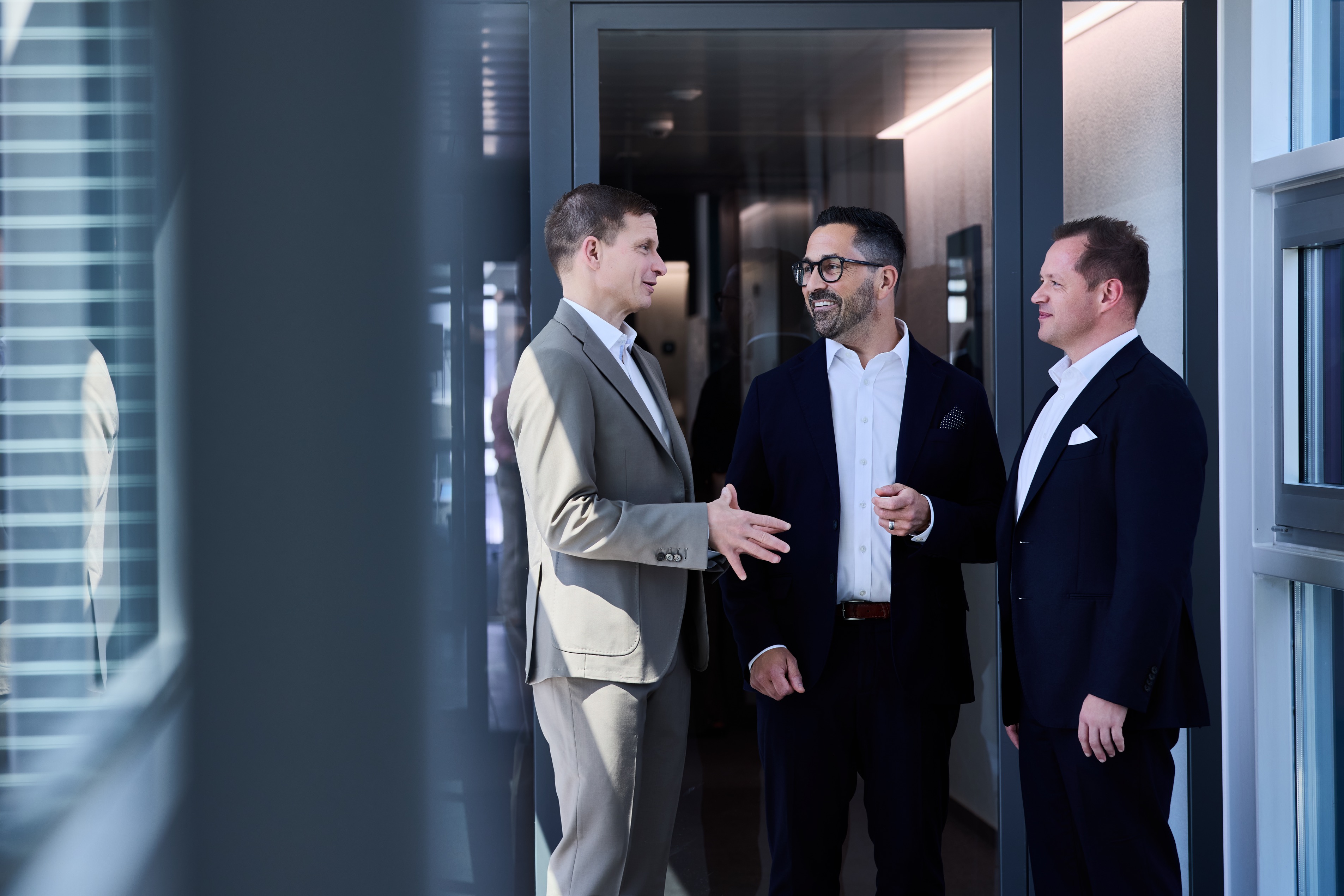 Trois hommes en costume discutent dans l'entrée d'un bureau.