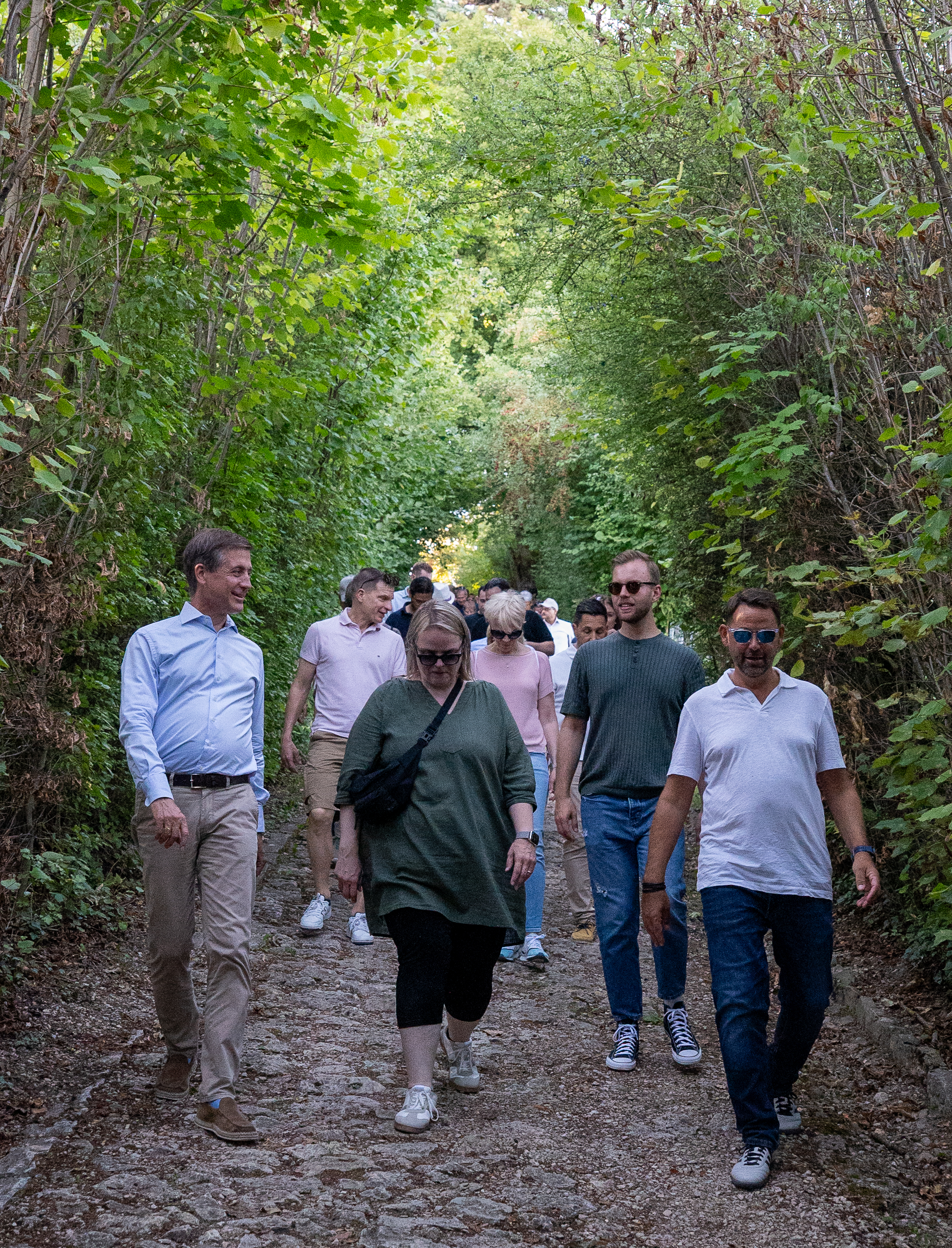Un groupe de personnes marchant ensemble sur un étroit sentier pavé bordé d'arbres.