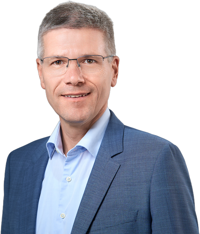 Ein Mann mittleren Alters mit kurzen Haaren und Brille, der ein blaues Hemd und einen blauen Blazer trägt.
