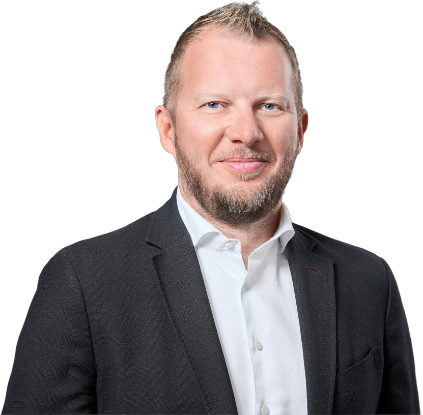 Ein Mann mittleren Alters mit kurzen Haaren und Bart, der ein weißes Hemd mit Kragen und einen dunklen Blazer trägt.