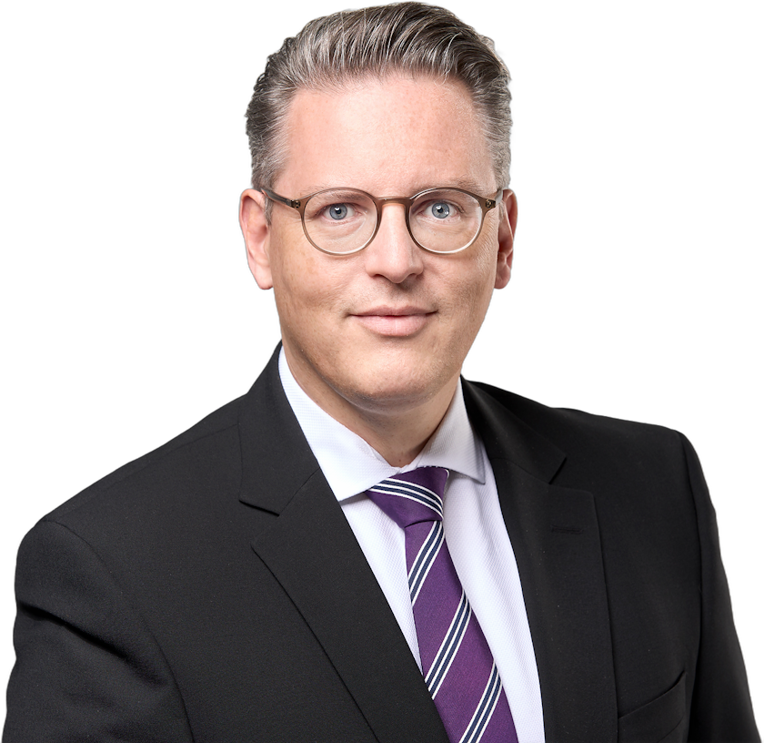 Ein Mann, der einen schwarzen Anzug, ein weißes Hemd und eine violett gestreifte Krawatte trägt und eine Brille trägt.