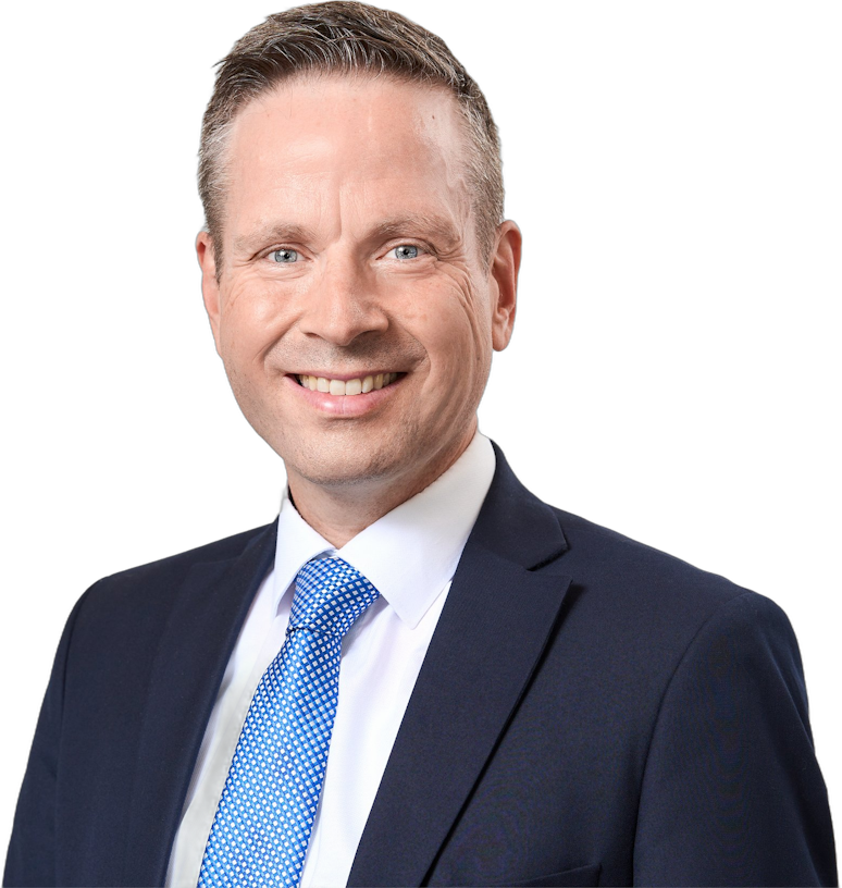 Ein Mann im Anzug und mit einer blau gemusterten Krawatte, der in die Kamera lächelt.