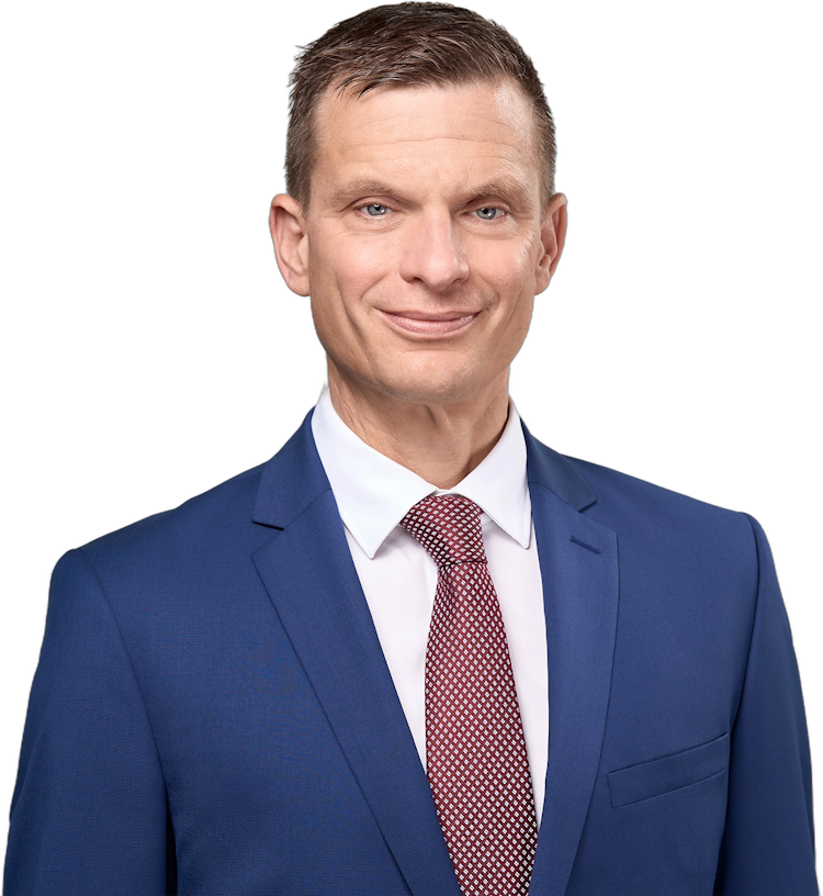 Ein Mann mittleren Alters in einem blauen Anzug, einem weißen Hemd und einer gemusterten roten Krawatte, der vor einem weißen Hintergrund lächelt.
