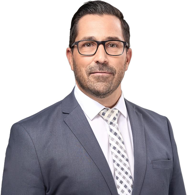 Ein Mann mittleren Alters mit dunklem Haar und Brille, der einen grauen Anzug und eine weiß gemusterte Krawatte trägt.