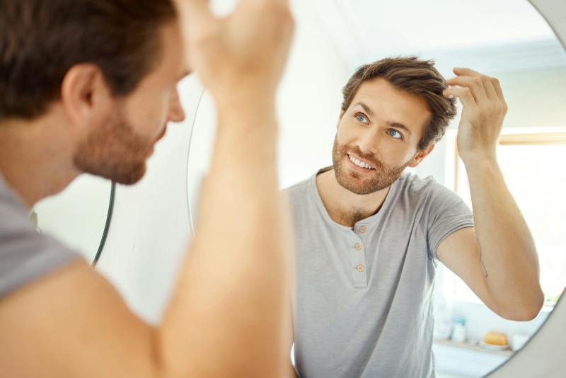 Man looks in mirror at hair happy