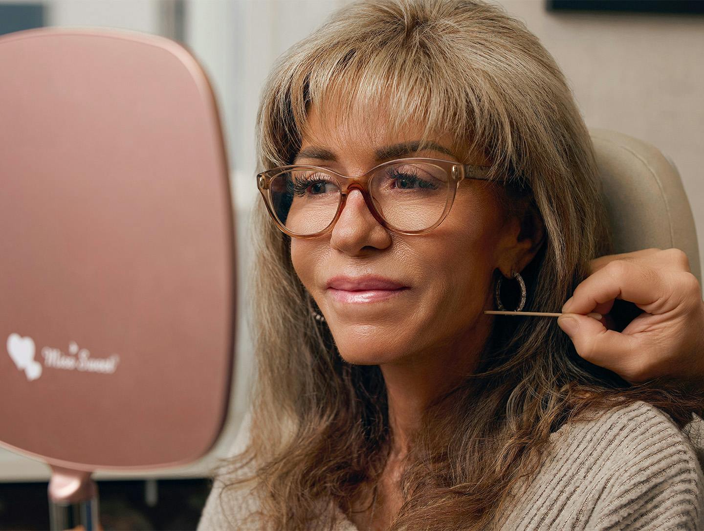 woman looking into a hand mirror while the doctor is pointing at her face