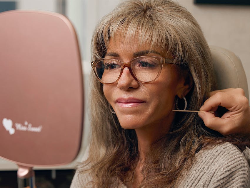 woman looking into a hand mirror while the doctor is pointing at her face