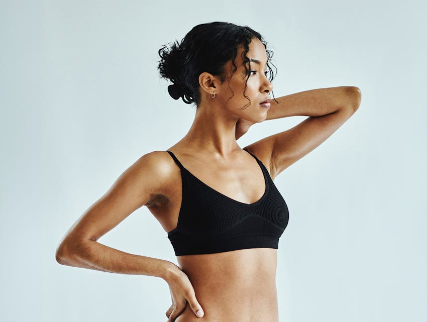 woman in a black bra, holding her hand on her hips and behind her head