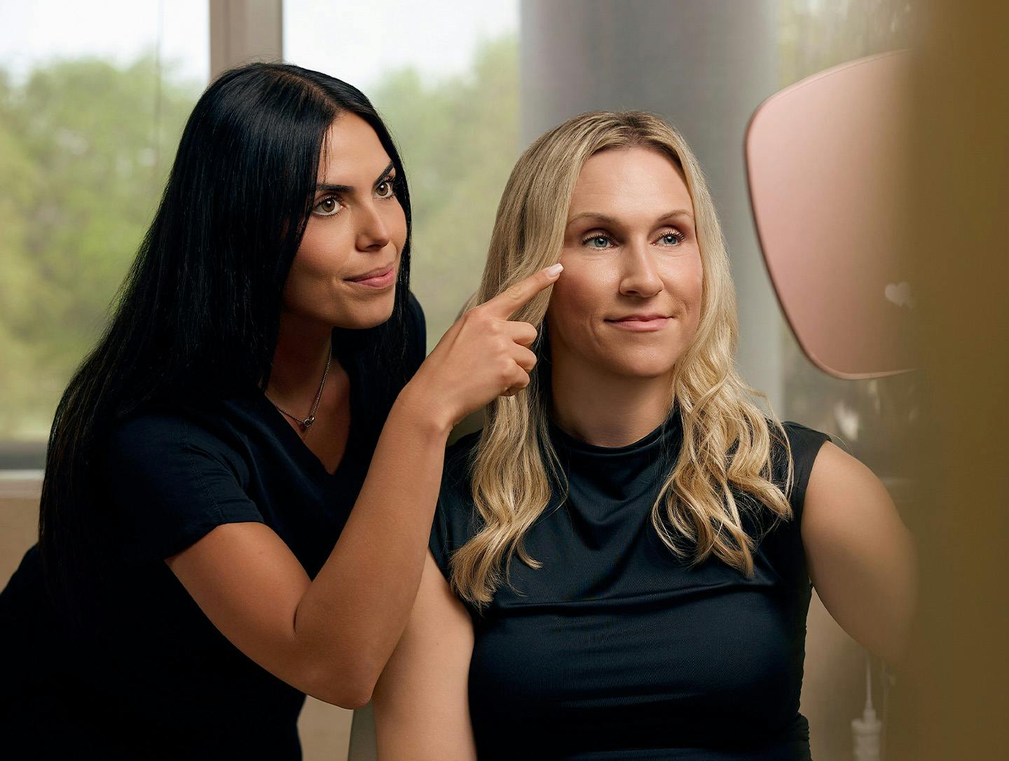nurse pointing at a woman's face while they look into a hand mirror