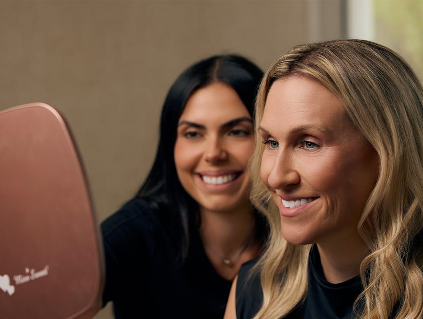 two women smiling into a hand mirror