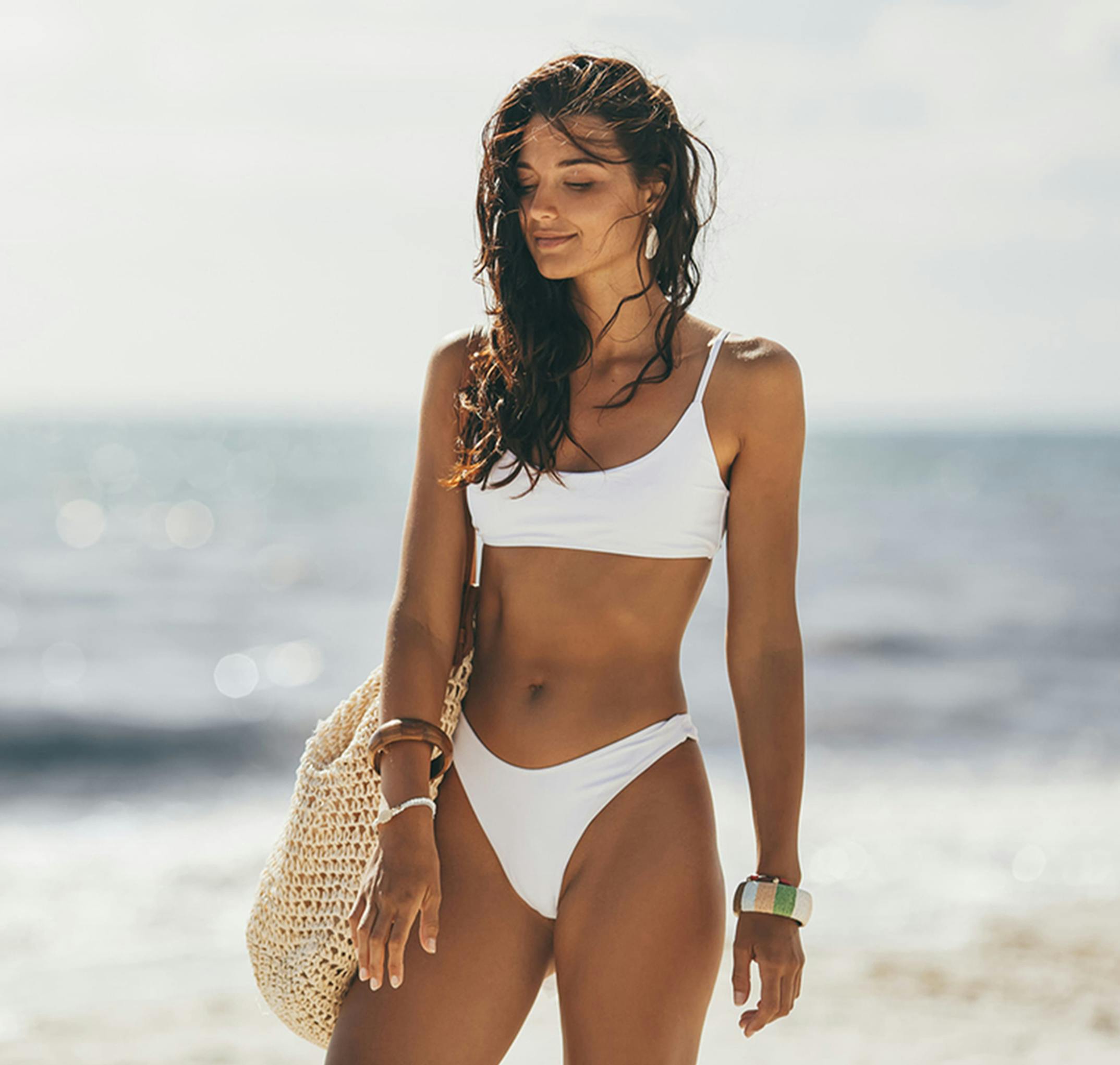 woman standing on a beach in a white bikini