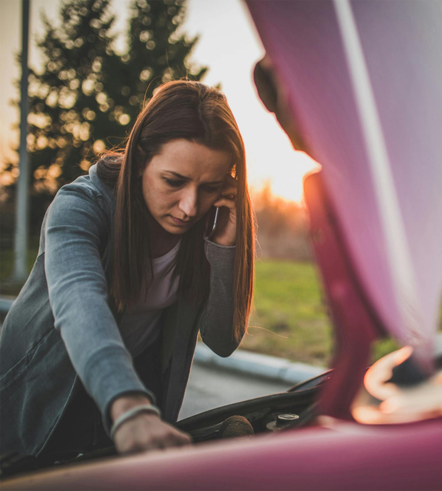 woman on the phone, looking under the hood of a car