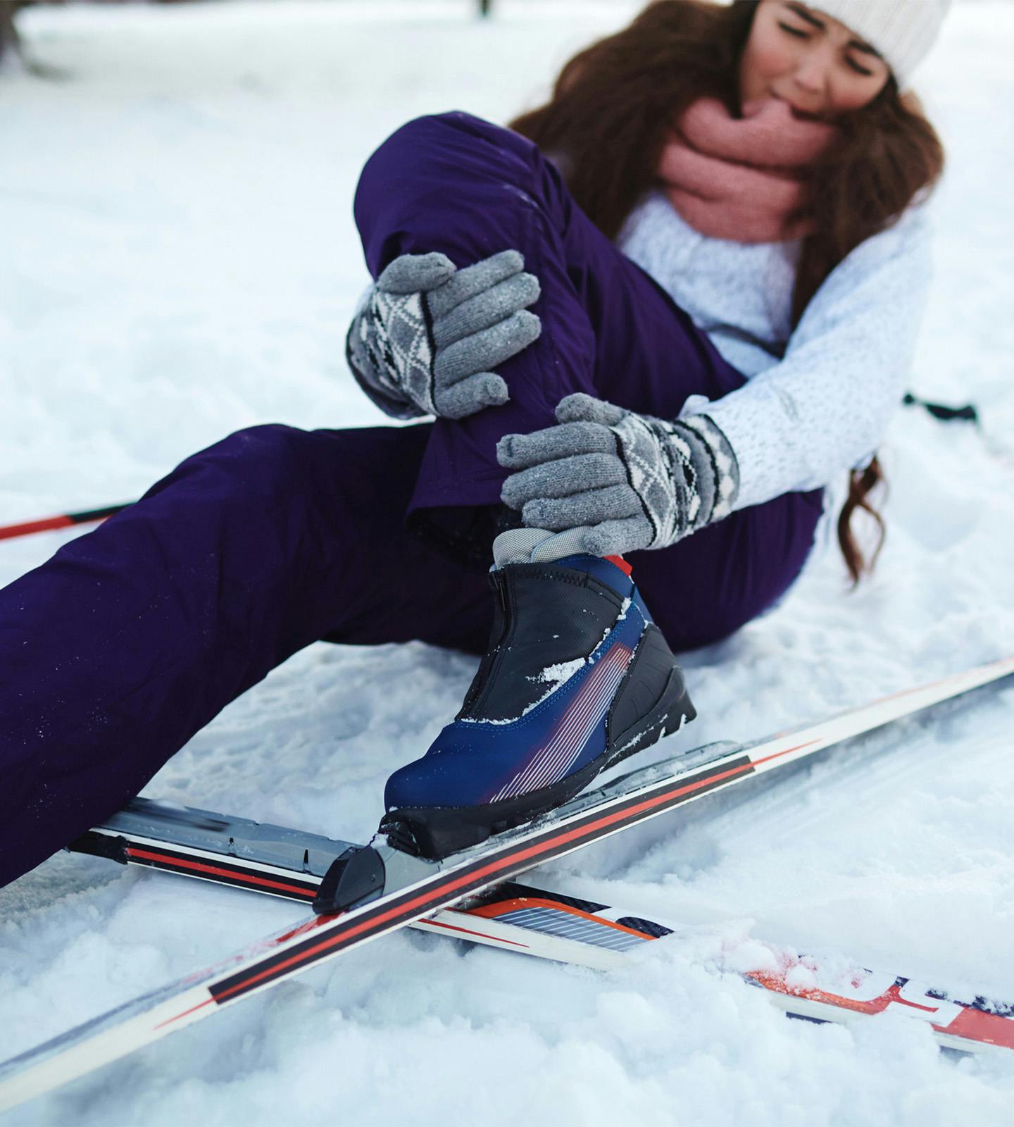 woman holding her leg in pain after falling off her skis