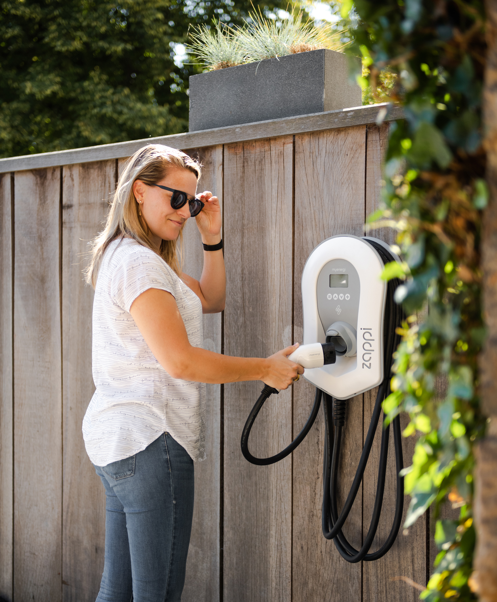 Un client à côté d'un chargeur mural pour véhicules électriques « myenergi Zappi » installé par 50Five.