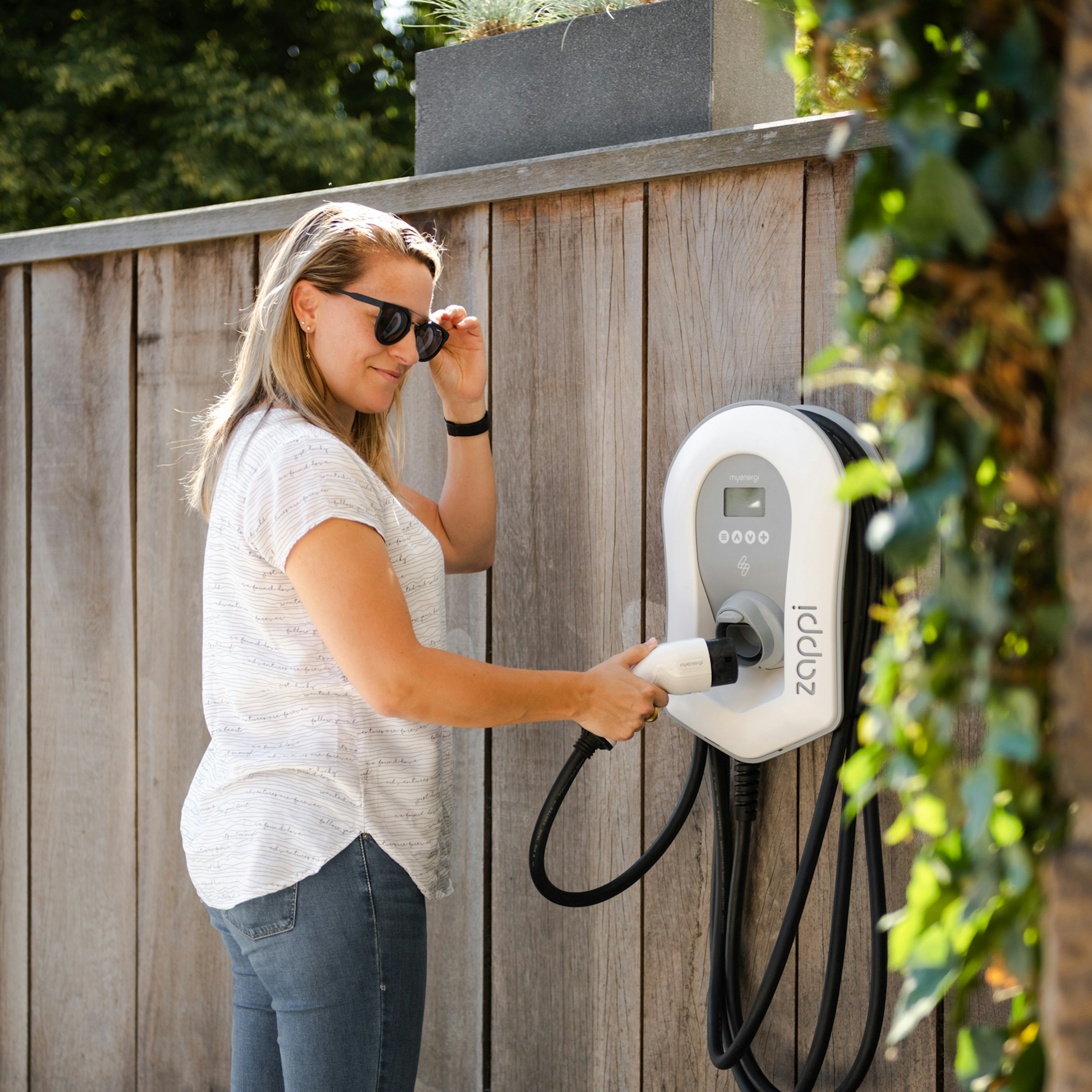 Un client à côté d'un chargeur mural pour véhicules électriques « myenergi Zappi » installé par 50Five.