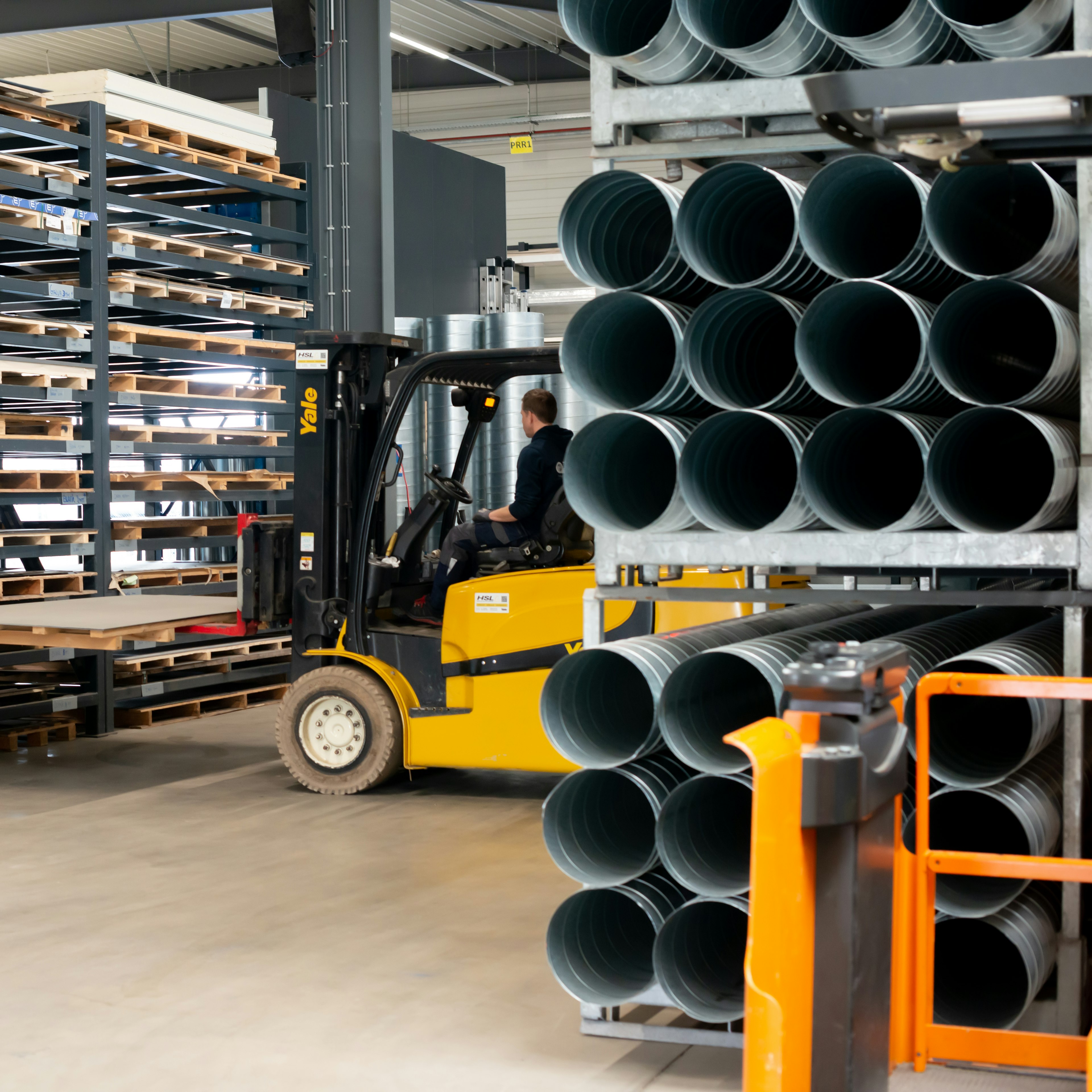A TM Technics technician operates a coil-forming line beside a branded banner, with steel coils stored above and two feed reels numbered 1 and 2.