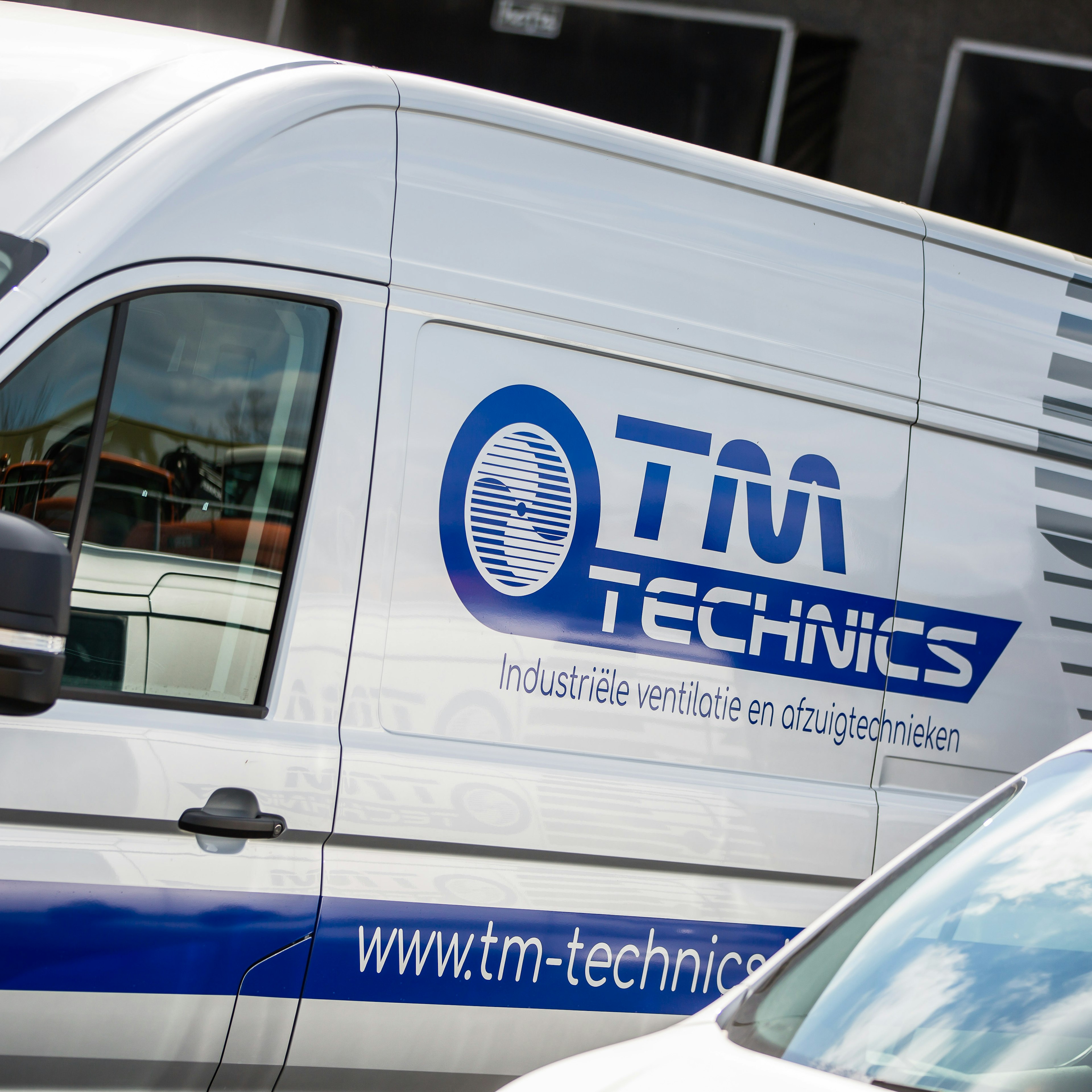 Vue de profil d'une camionnette blanche TM Technics, sur laquelle figurent le logo et le slogan « industriële ventilatie en afzuigtechnieken »