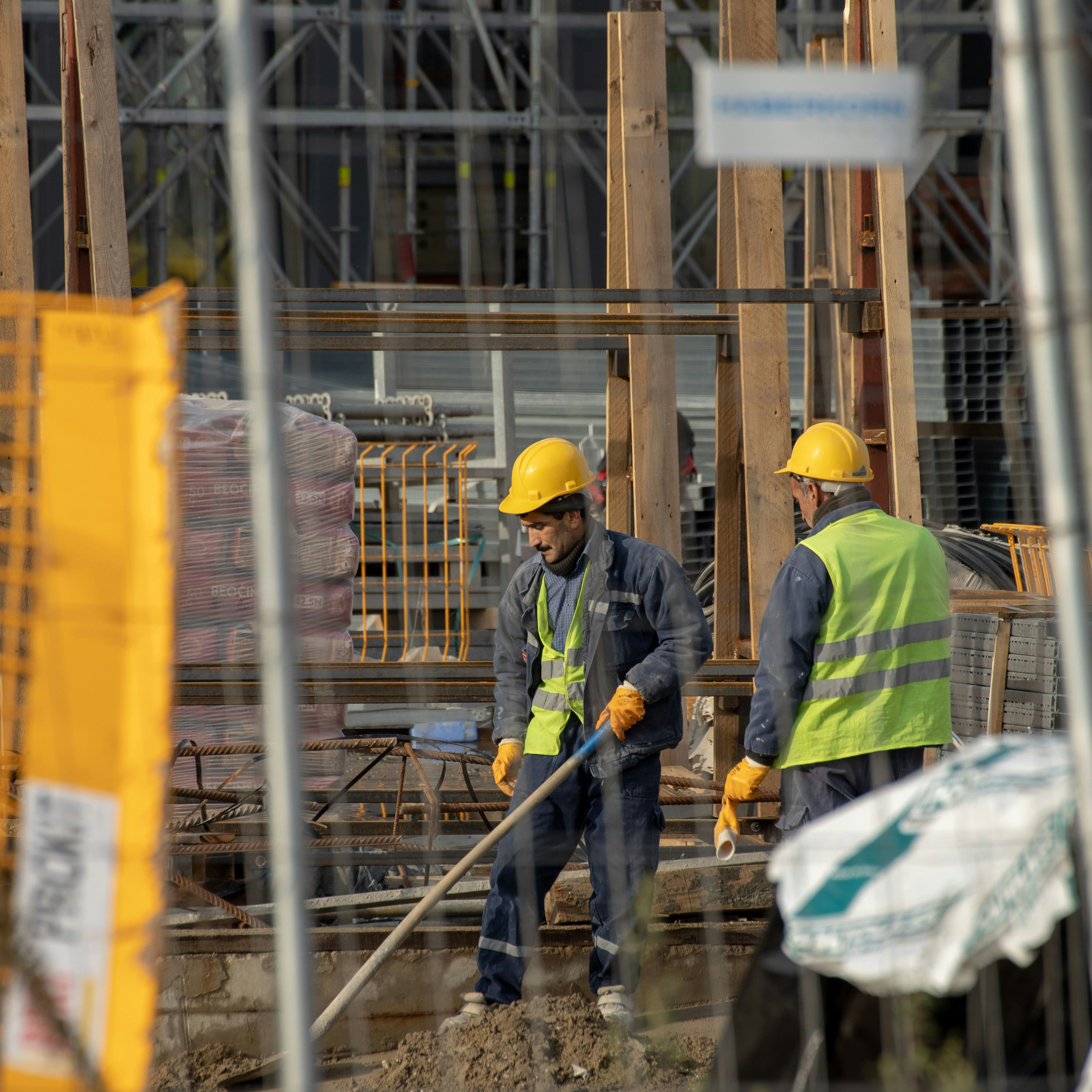 Des ouvriers du bâtiment en gilets haute visibilité derrière la clôture du chantier