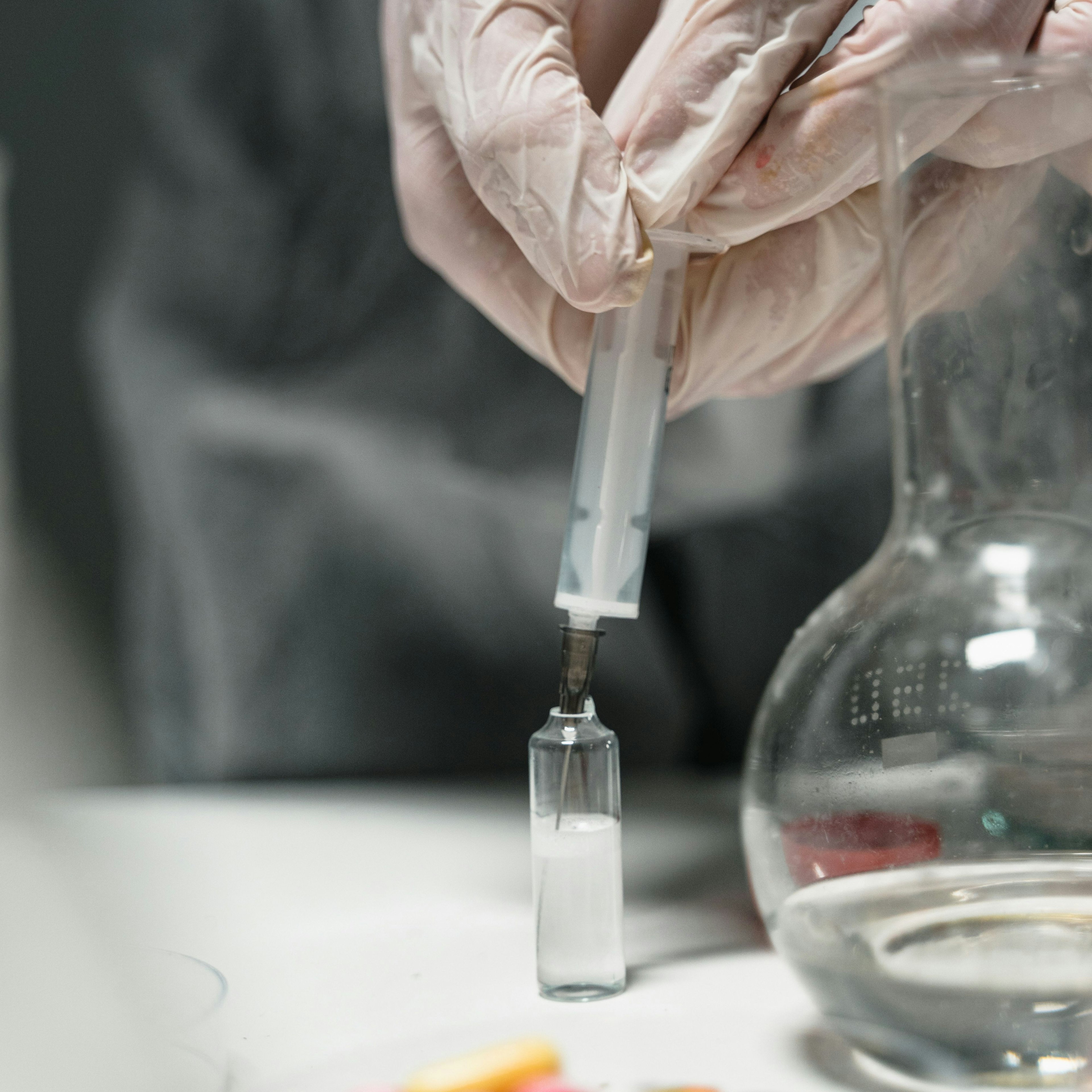 Un technicien de laboratoire en train de pipeter un liquide dans un flacon dans le cadre de la recherche pharmaceutique.