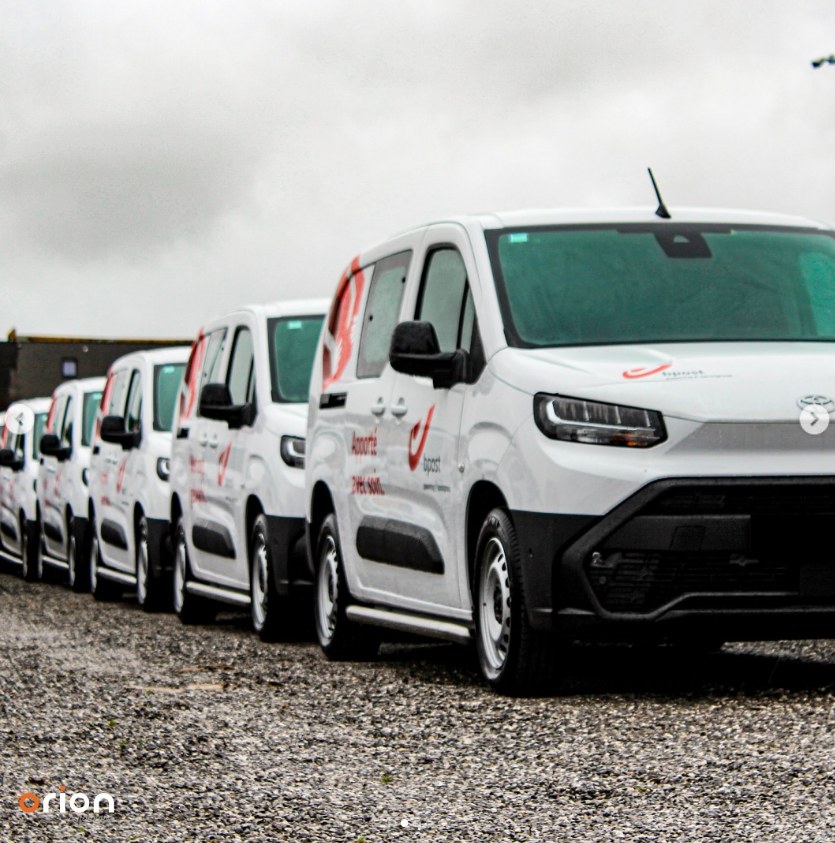 L'équipe d'Orion Automotive pose devant des véhicules aux couleurs de la marque, sous le logo de l'entreprise, à l'entrée de ses locaux.