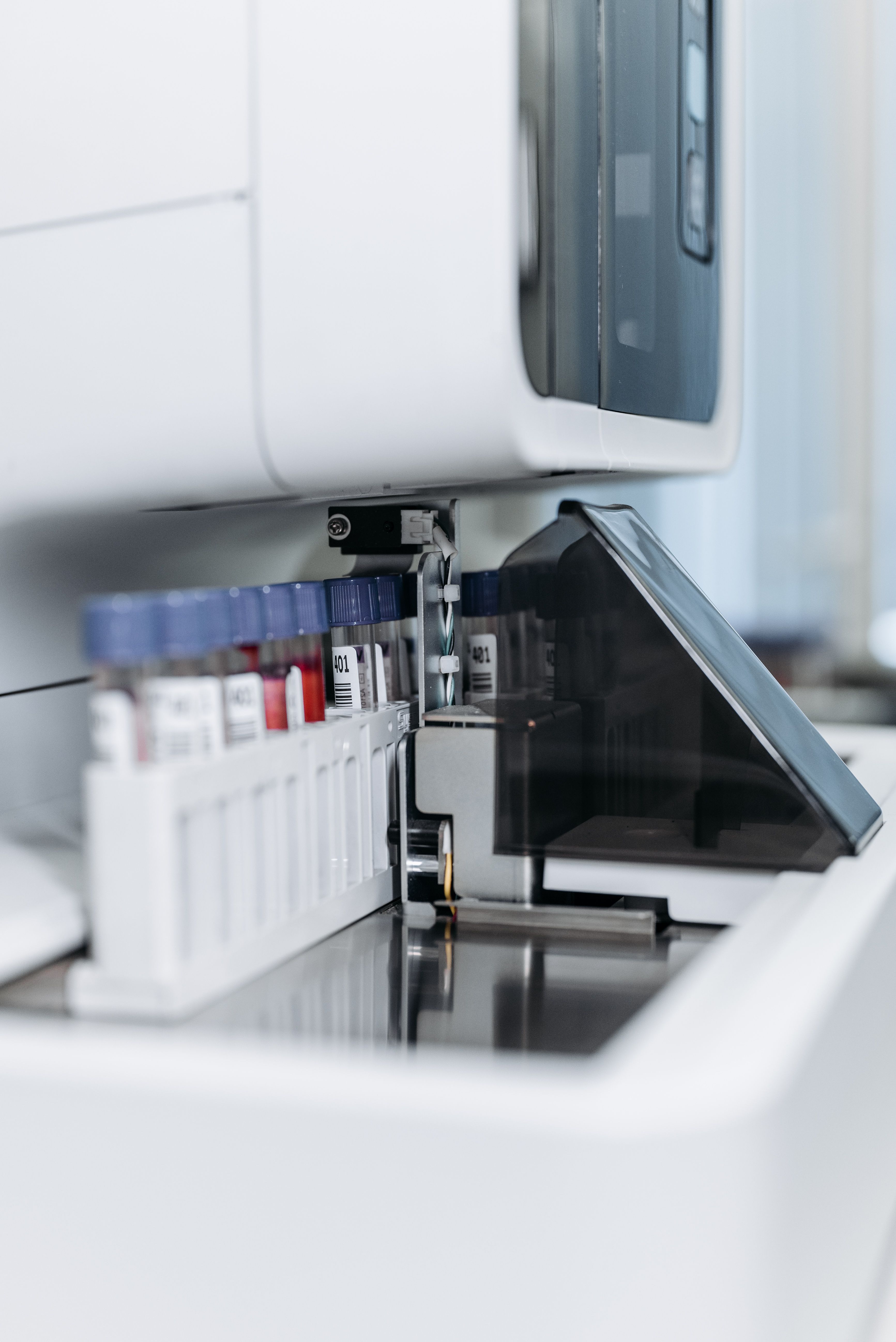 Gros plan sur un analyseur de laboratoire automatisé équipé d'un plateau de chargement contenant des tubes à échantillons munis de codes-barres, dont l'un est muni d'un bouchon bleu et l'autre contient un liquide rouge.